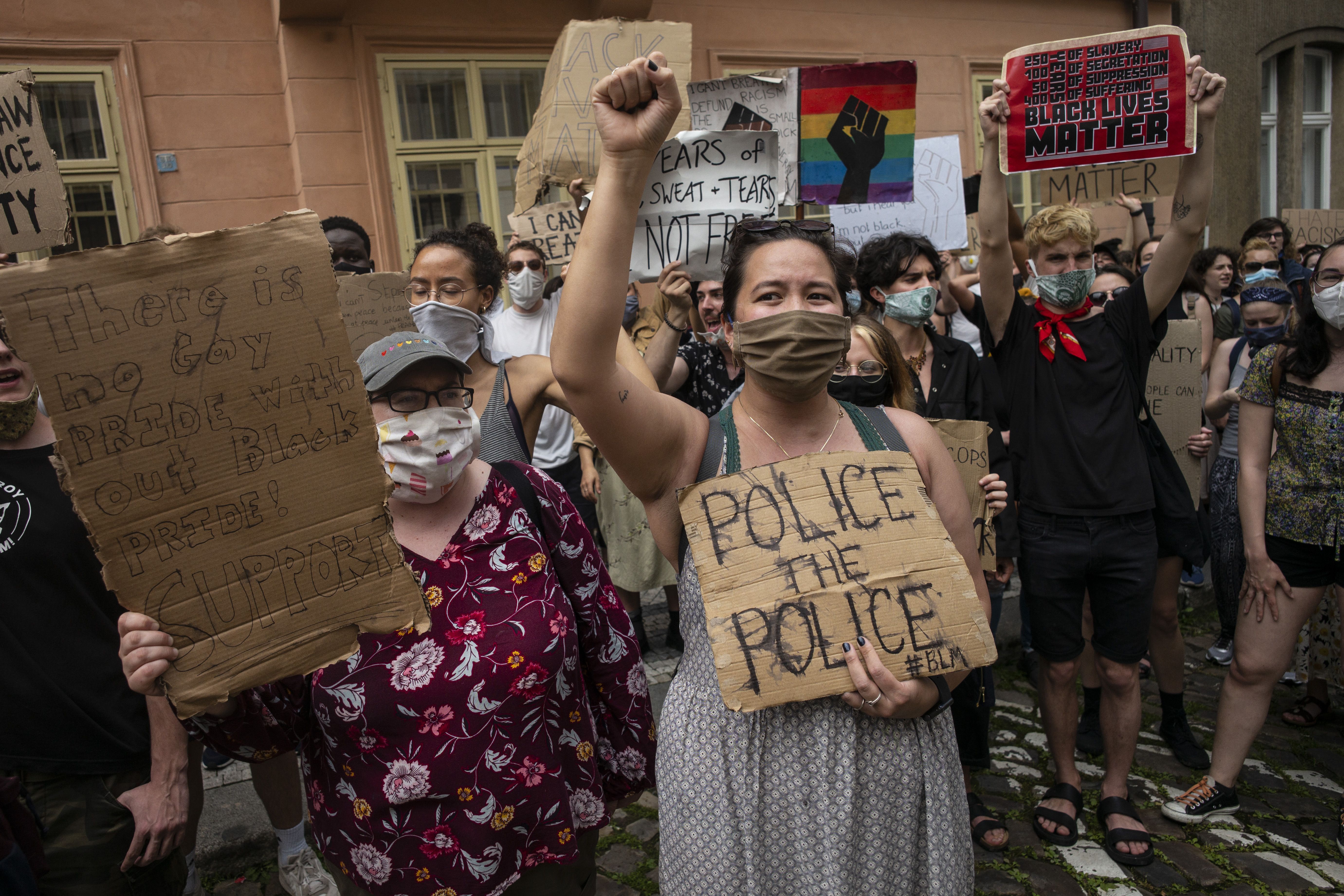 A masked woman holds a sign that reads "police the police" 