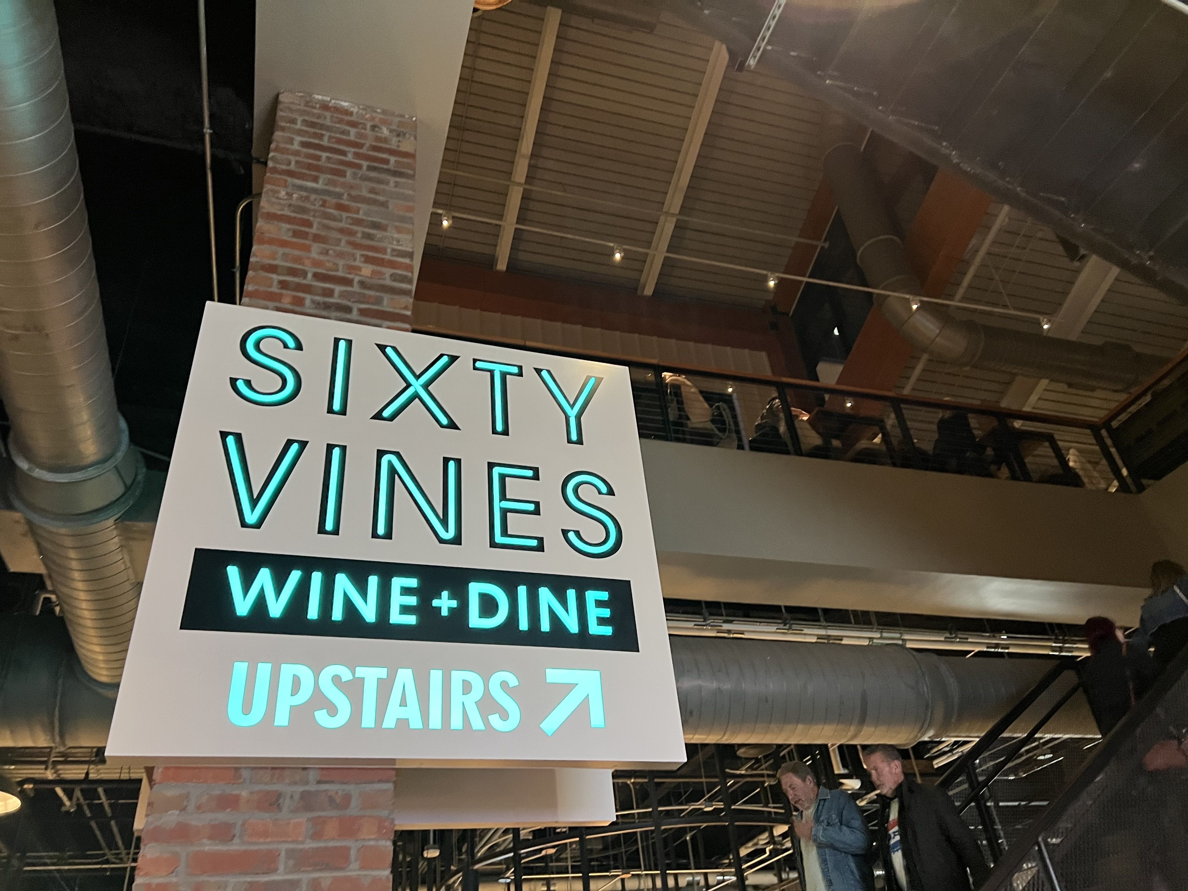 fluorescent sign that says "Sixty Vines Wine + Dine Upstairs"