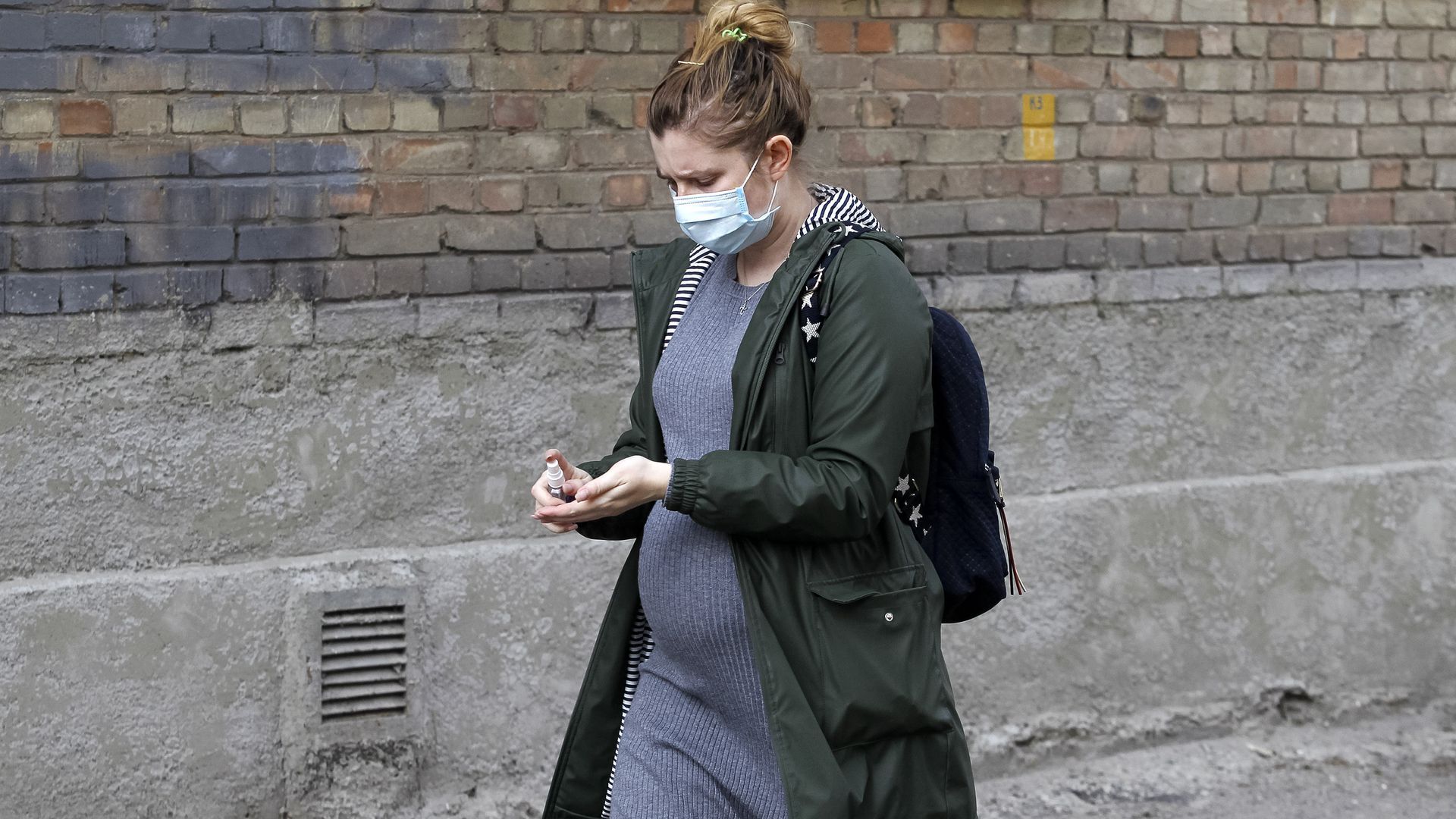 A pregnant woman walks down a street while wearing a surgical mask