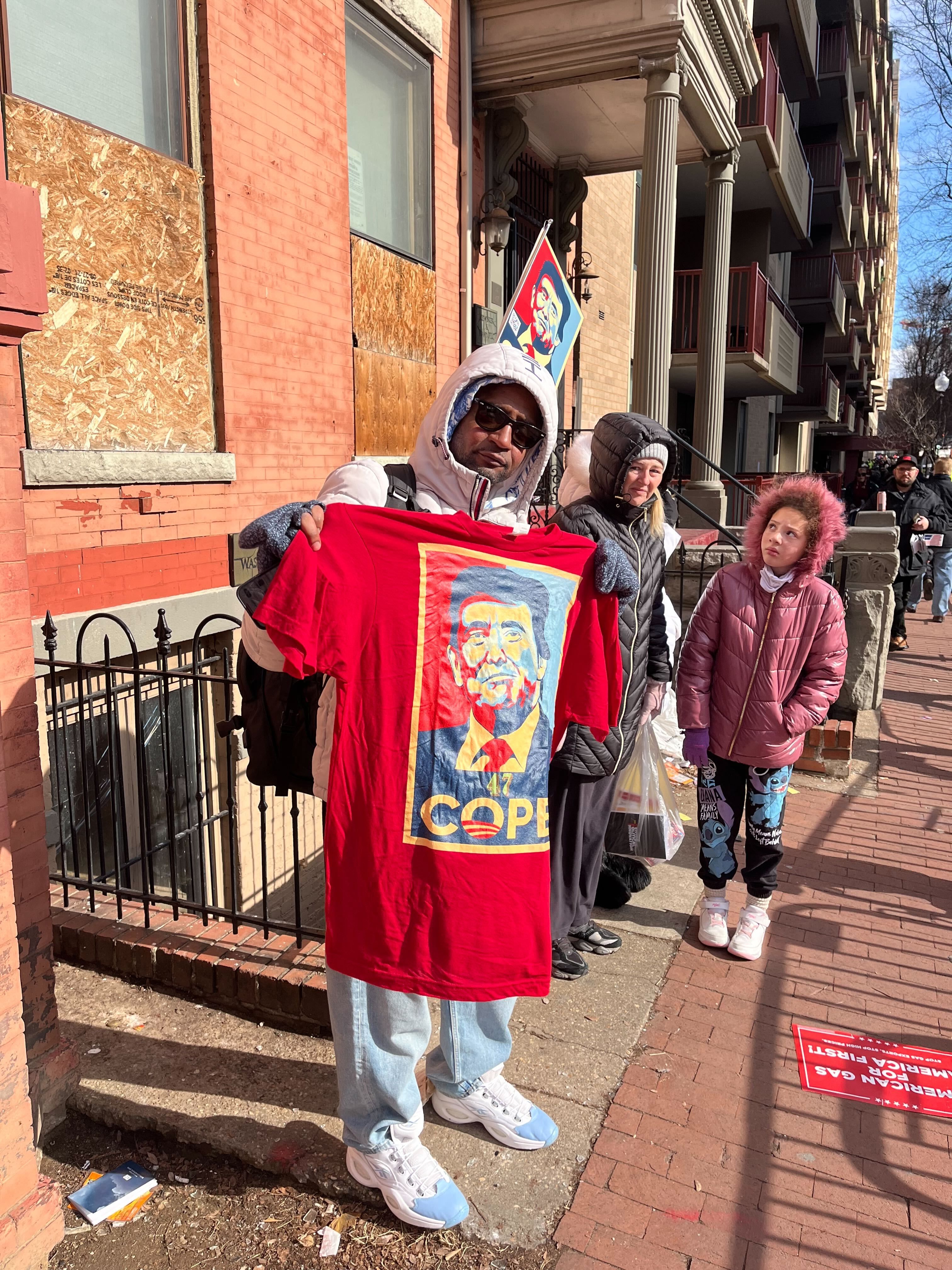A man holding a red t-shirt with a picture of Donald Trump and the slogan "Cope" underneath it.