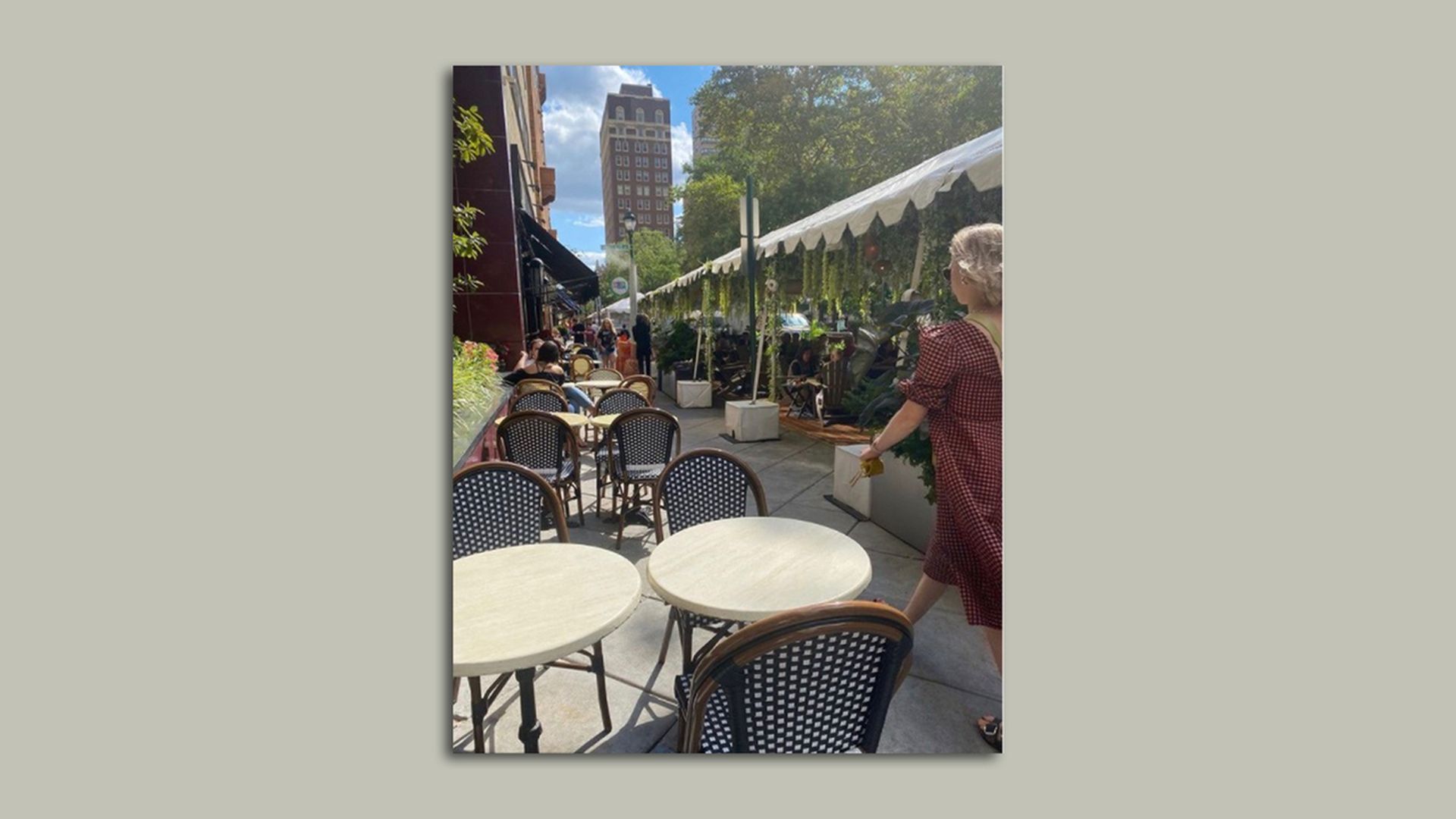 A woman walks along a sidewalk in Rittenhouse Square through Rouge restaurants tables and streetery. 