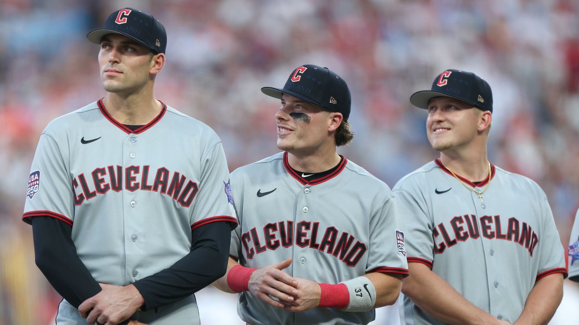 Three baseball players in gray jerseys and navy blue hats with red Cs