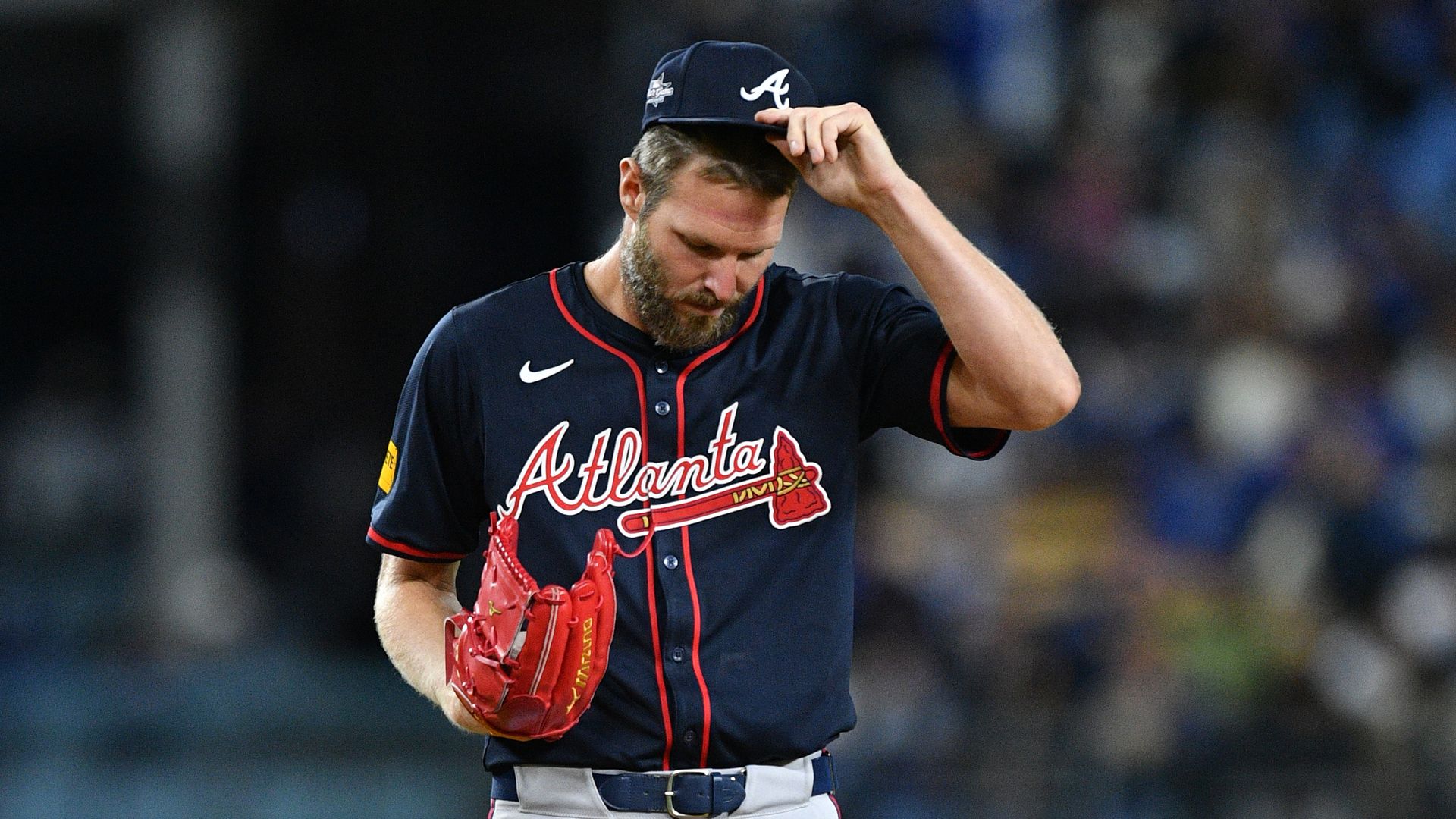 A man in a baseball uniform looks forlorn as he touches his hat