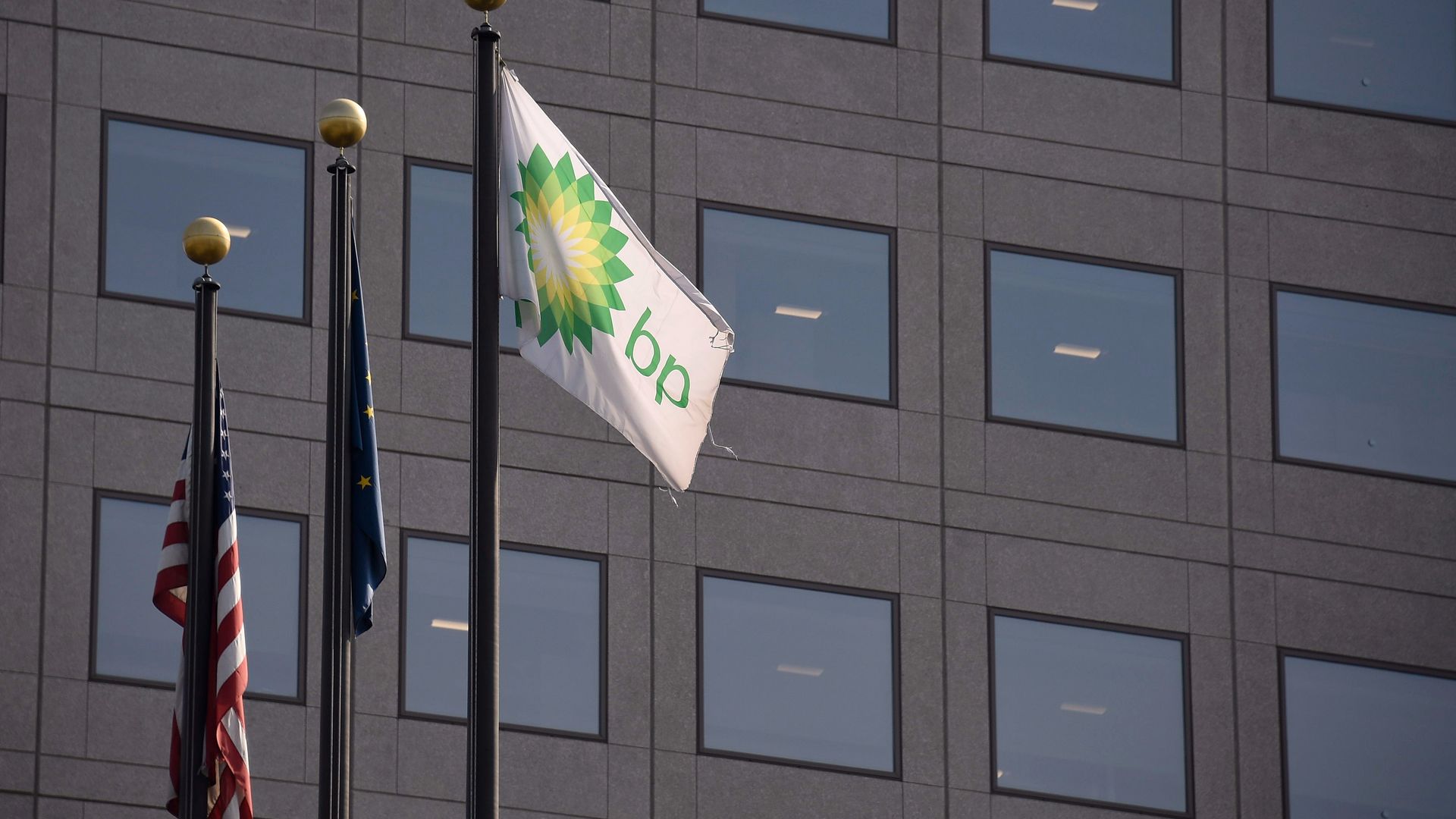 The American flag next to another flag and the flag of BP on a staff next to a building. 