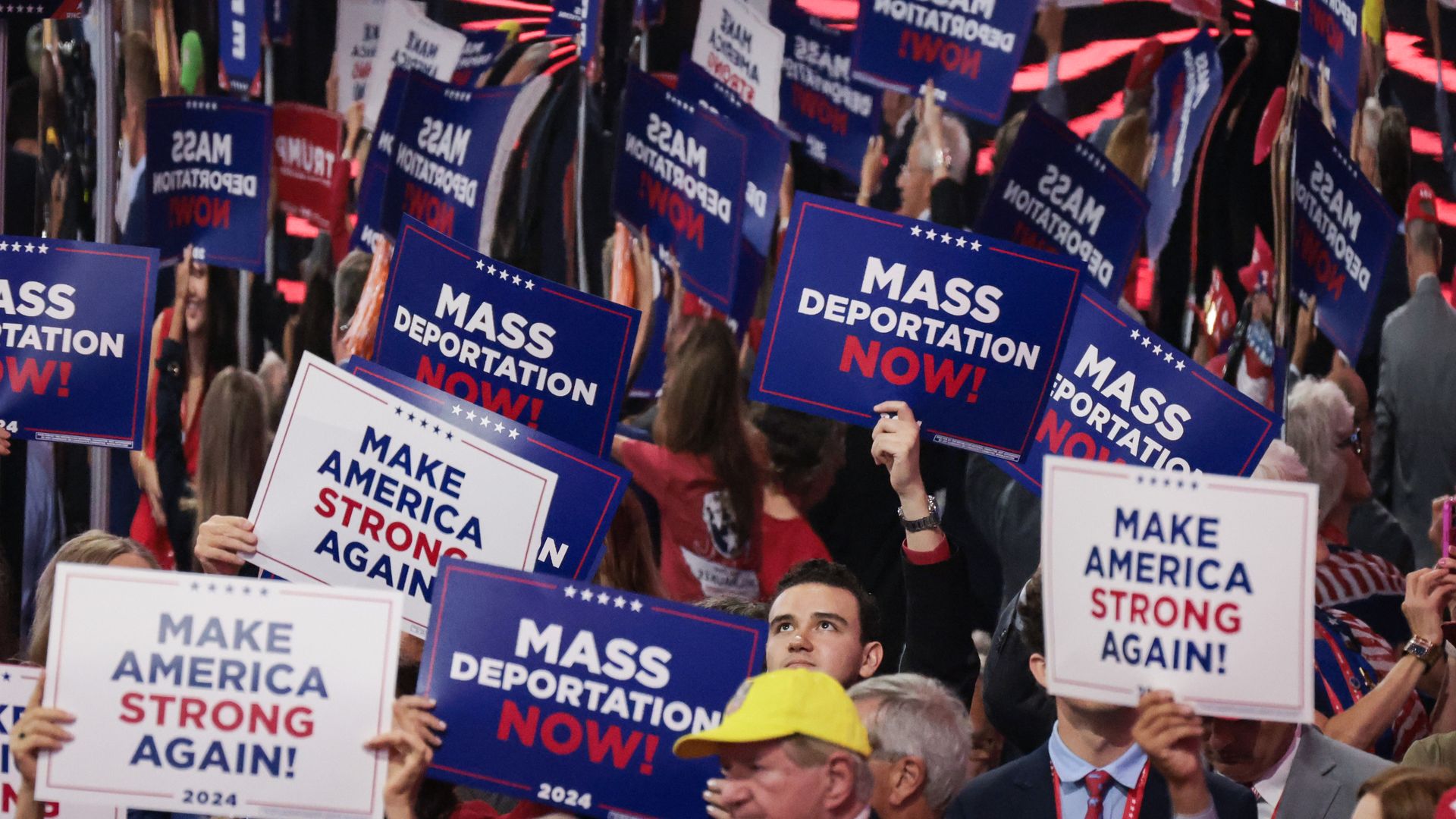 People hold signs that read "Mass Deportation Now" and "Make America Strong Again" at the 2024 Republican National Convention.