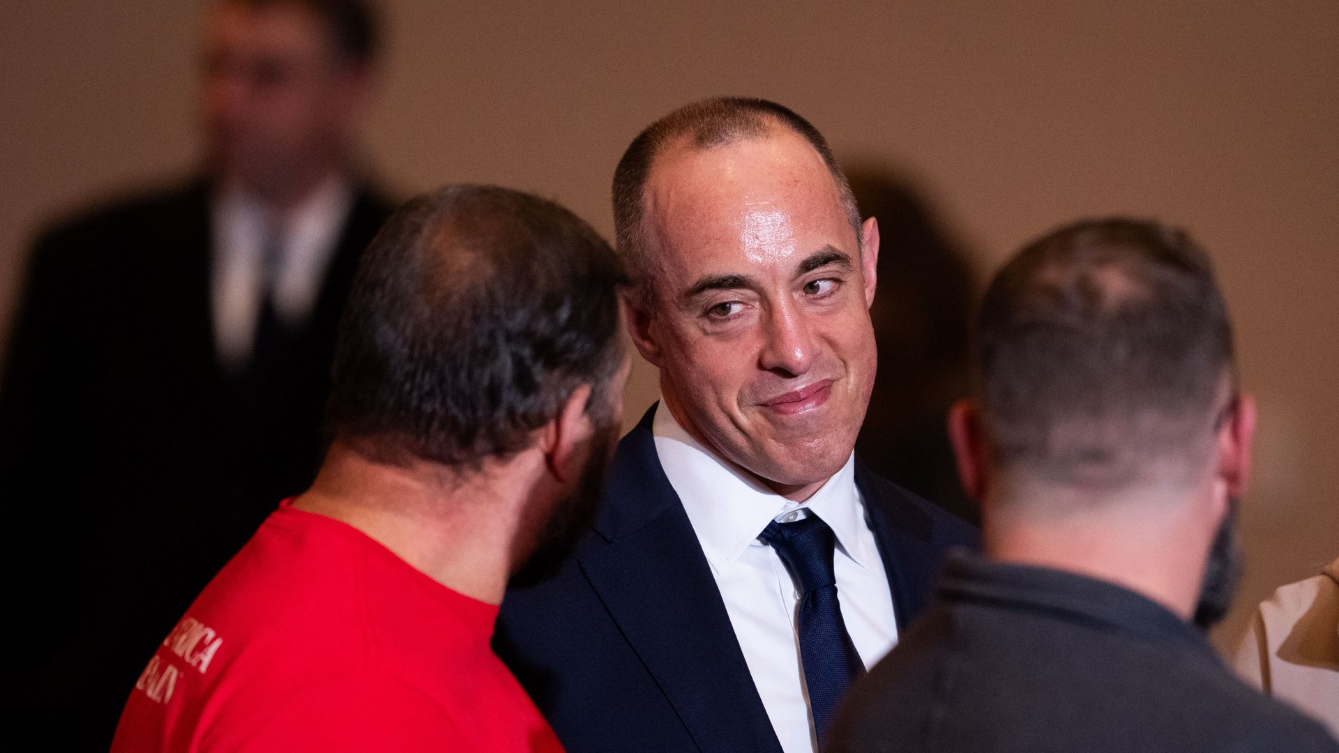 Emil Bove, wearing a dark jacket and tie with a white collared shirt,  smiles and listens while attending a speech delivered by President Trump, who is not pictured.
