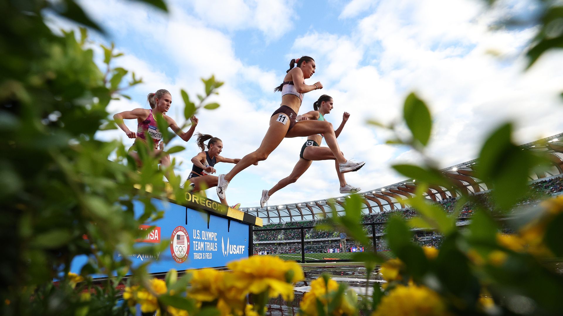 Multiple women hurdle over a barrier during a race. 