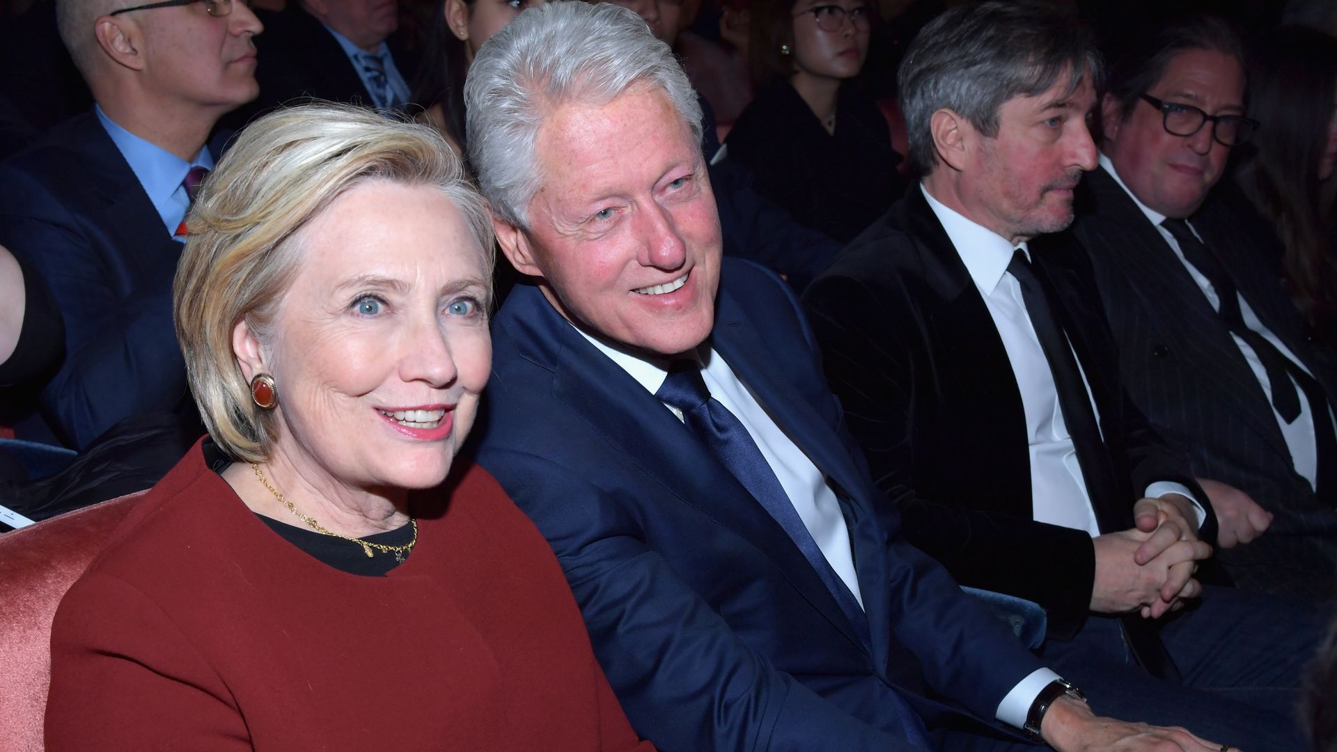 Hillary and Bill Clinton sitting next to each other and smiling at the camera