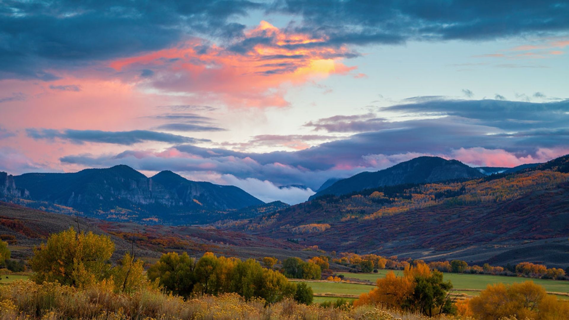 Scenic landscape view of Colorado mountains during sunset, featuring dramatic clouds and vibrant colors.