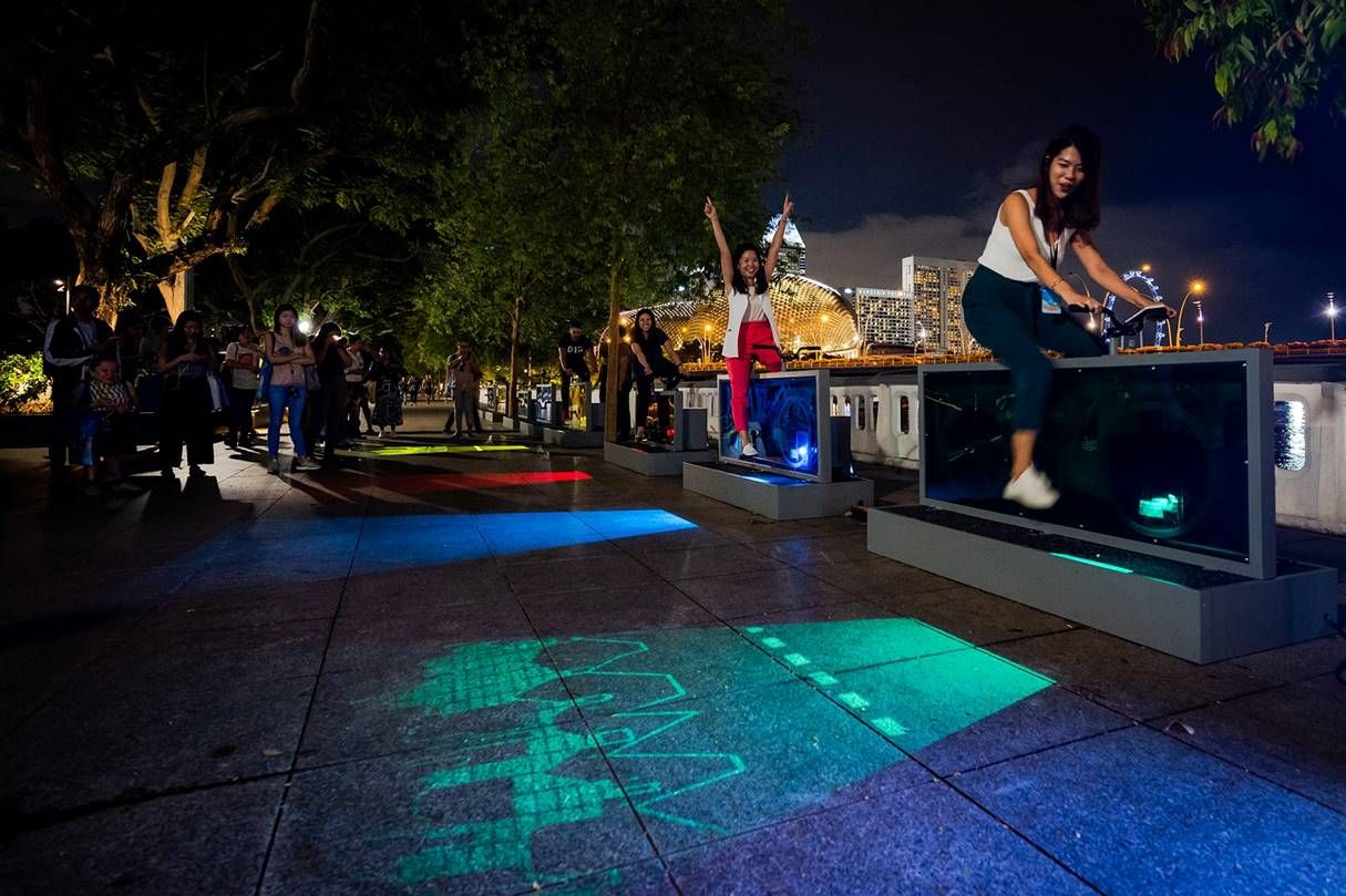 Two people in Singapore pedal on the Light Lane bicycle installation, producing images and music with the energy from their pedaling