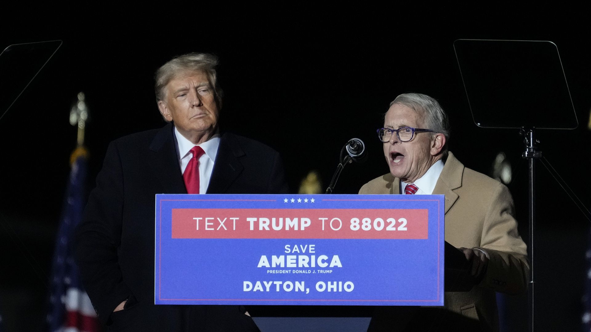 Ohio Governor Mike DeWine speaks at a Dayton political rally as former President Trump looks on.