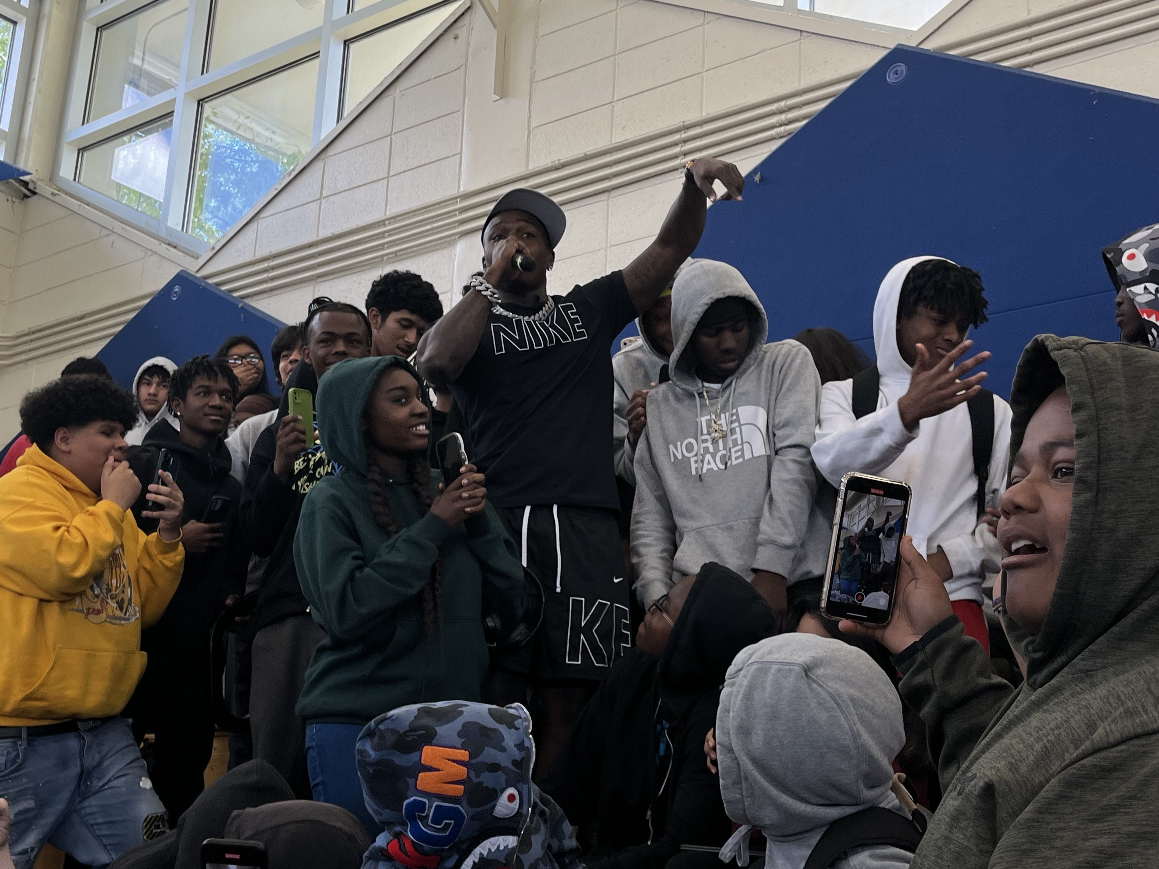 DaBaby in a high school gym surrounded by students