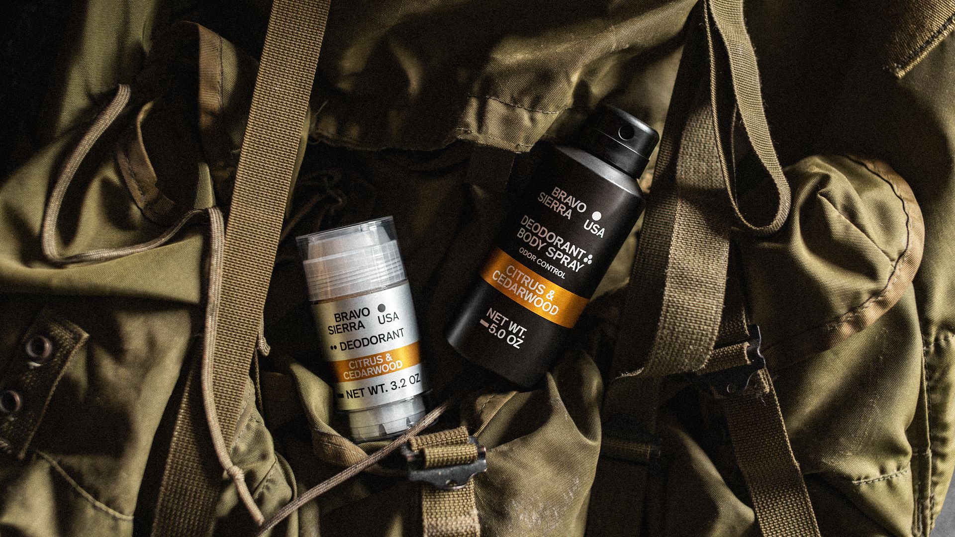 Two canisters, one silver and for deodorant and the other black and containing body spray, lay on top of a green duffle bag.