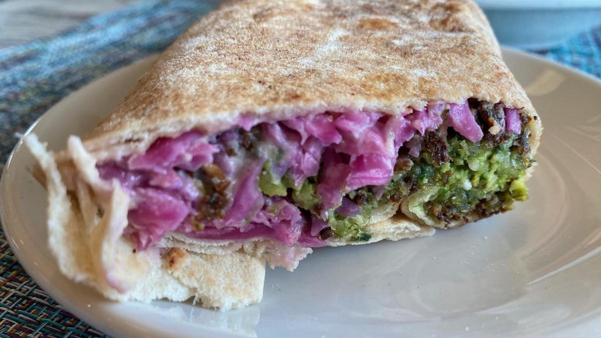 A pressed falafel sandwich with green and purple 