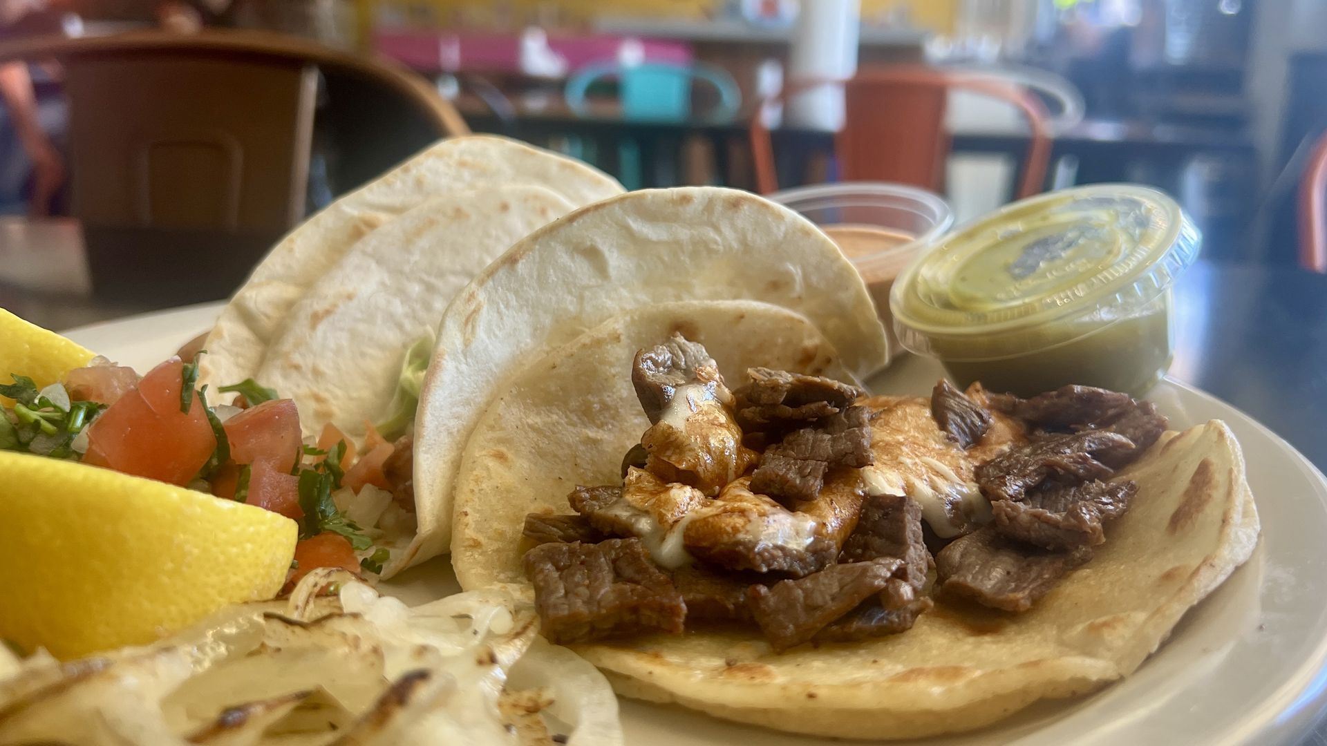 Three tacos on a plate with onions, limes and pico de gallo