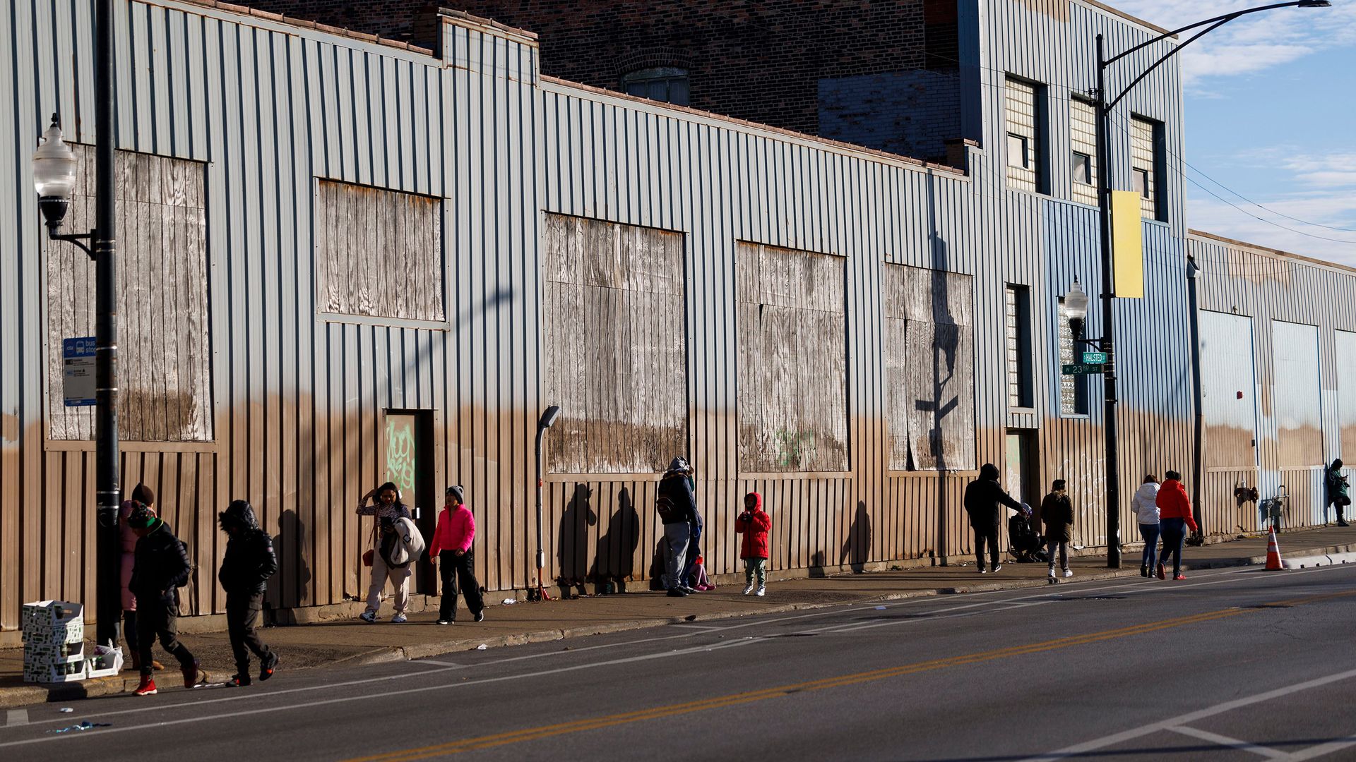 People stand and walk outside a migrant shelter on a sunny day in Chicago.