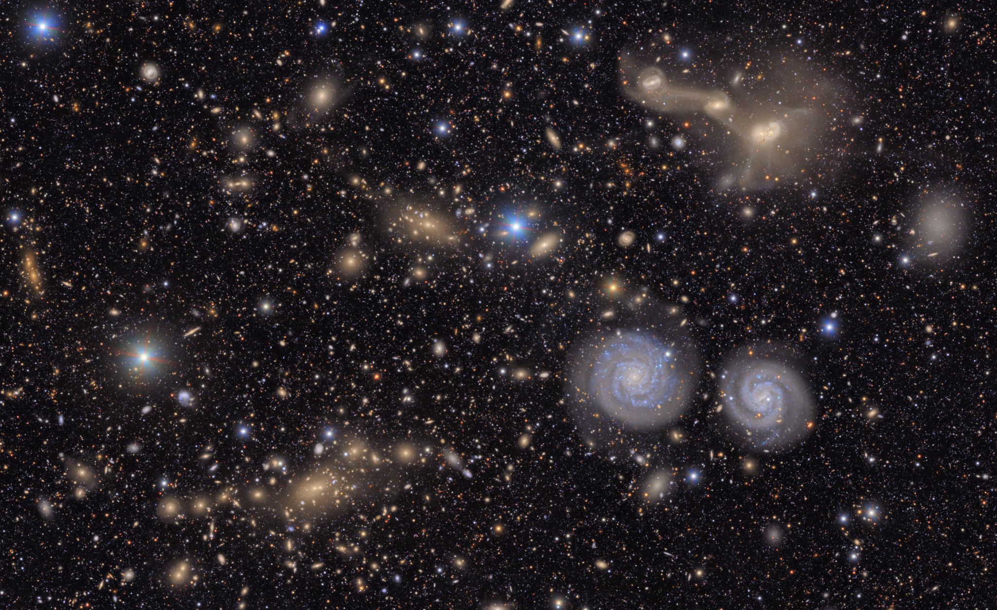 A deep-space view filled with thousands of stars and distant galaxies, including several bright spiral galaxies.