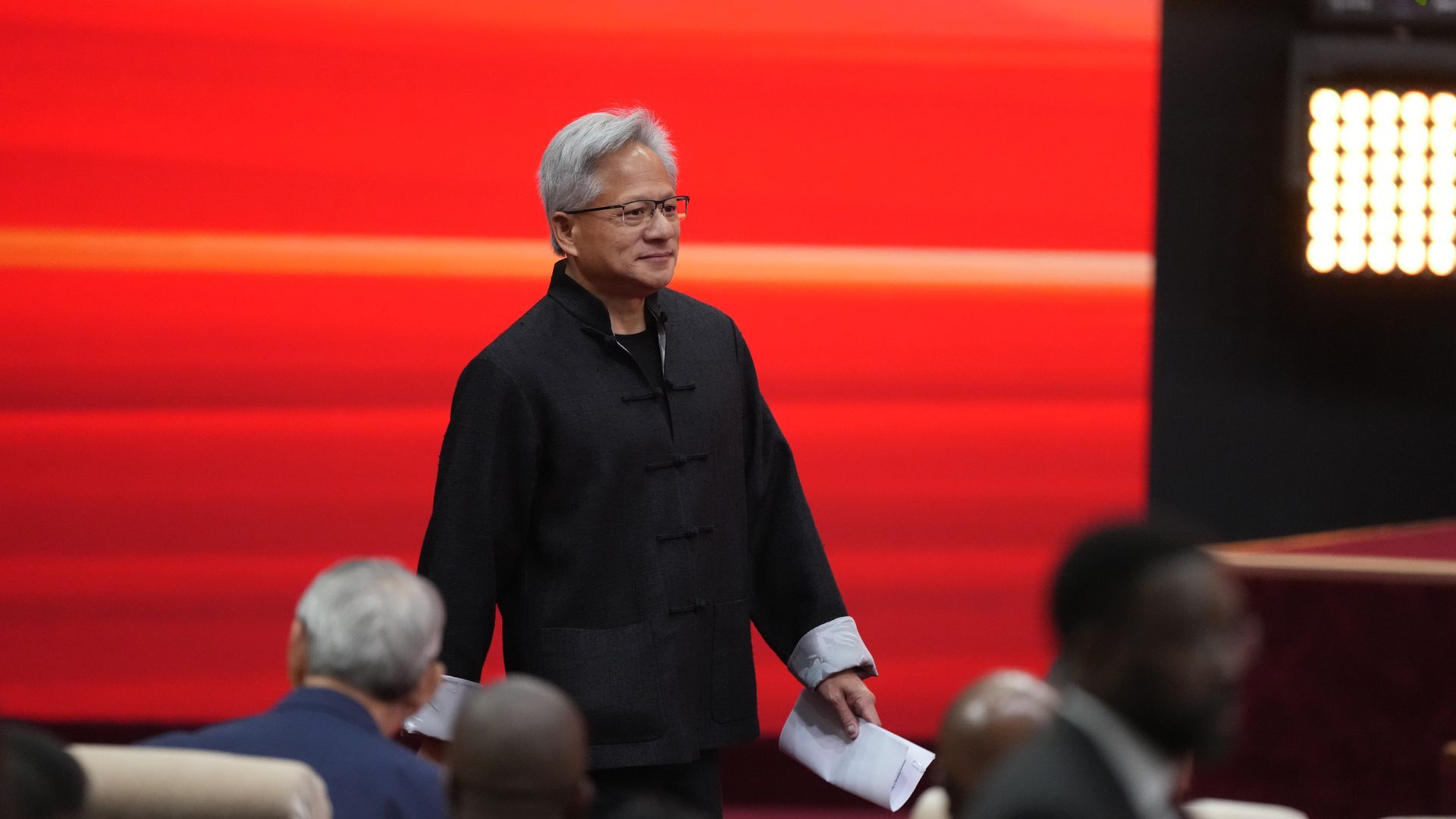 A man in a black shirt stands in front of a red screen with a paper folded in his left hand.
