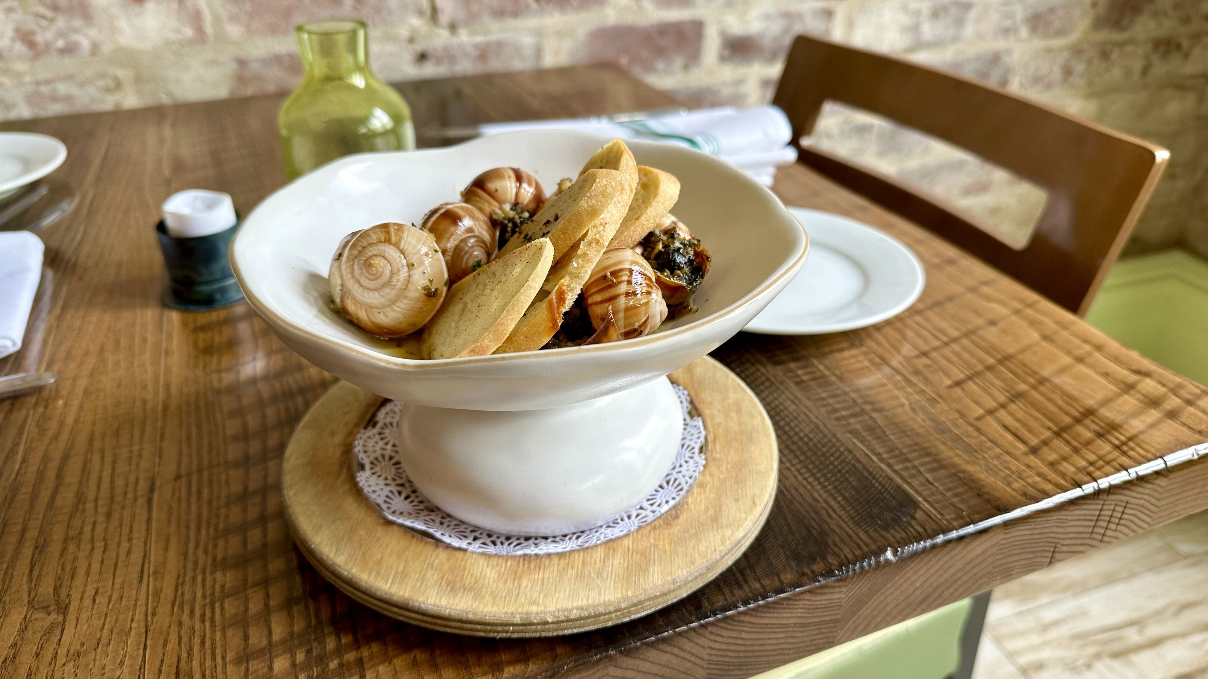 A pedastal bowl of escargot sits on a wooden tabletop.