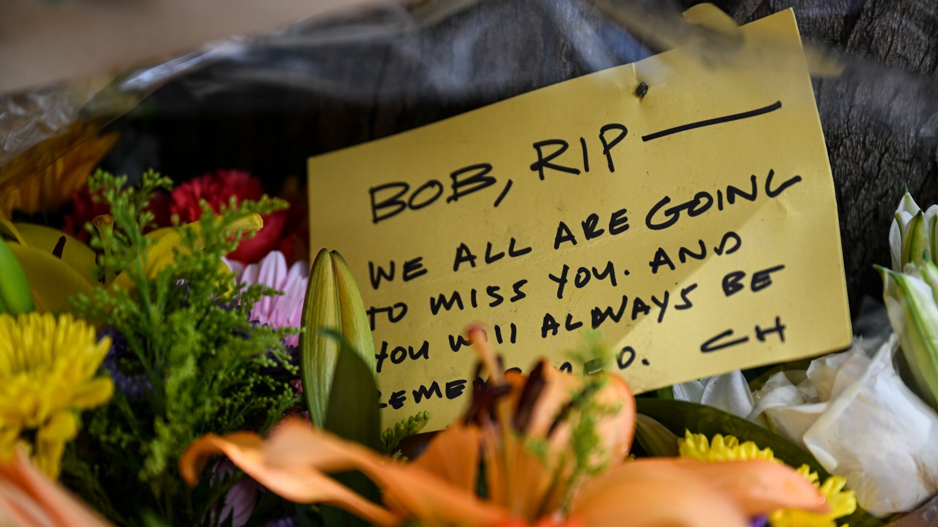 Photo of a note with the written words: "Bob, RIP — we all are going to miss you. And you will always be remembered." The note is surrounded by flowers.