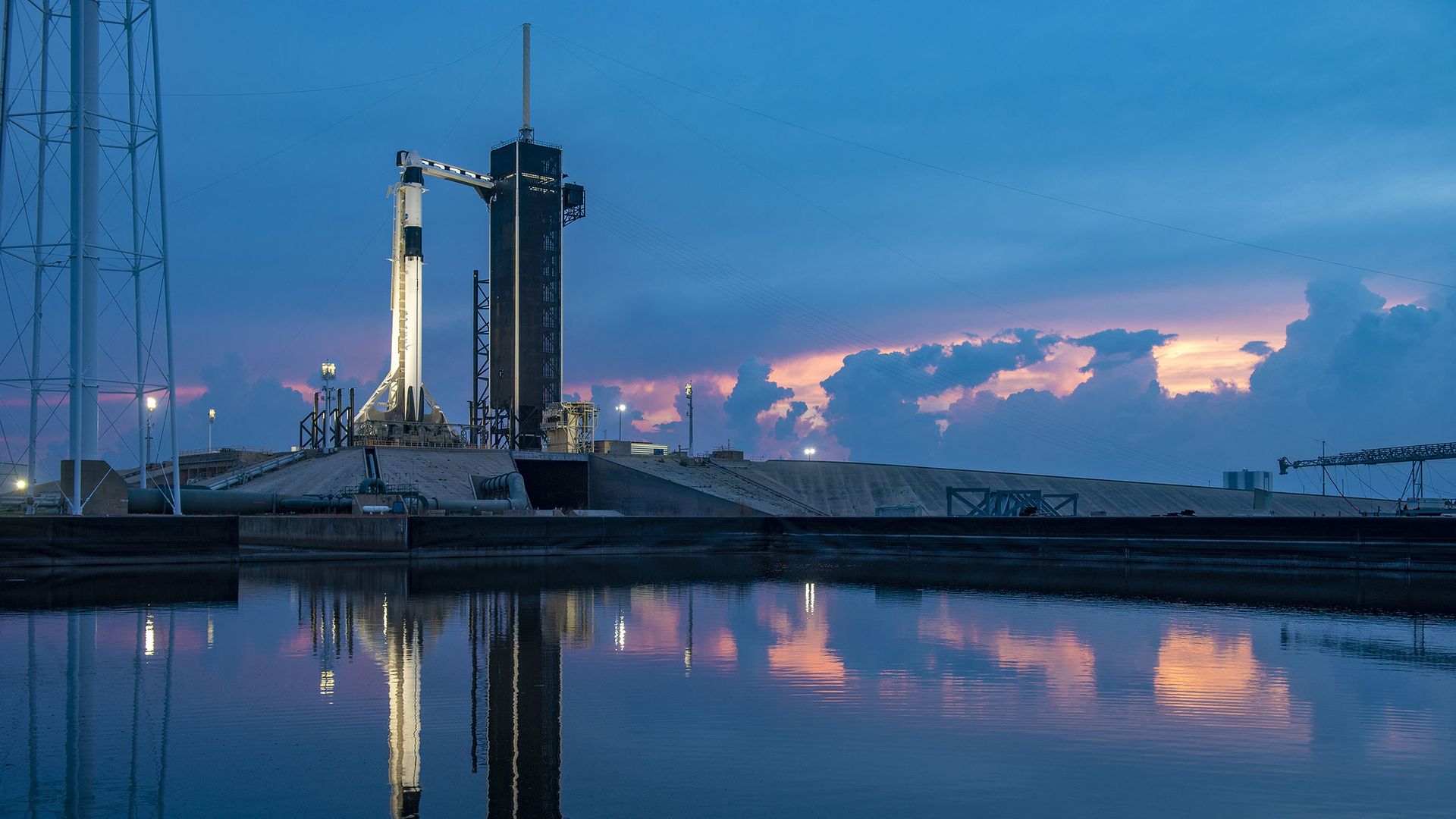 Cape Canaveral with a Falcon 9 rocket rising up into a dark sky above water