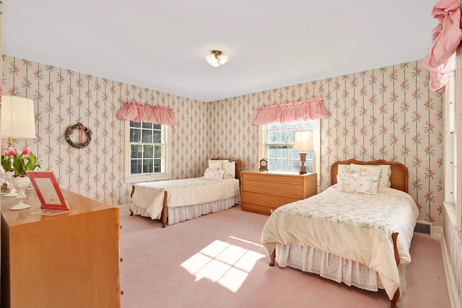 A bedroom with pink carpet, pink wallpaper and two small beds.