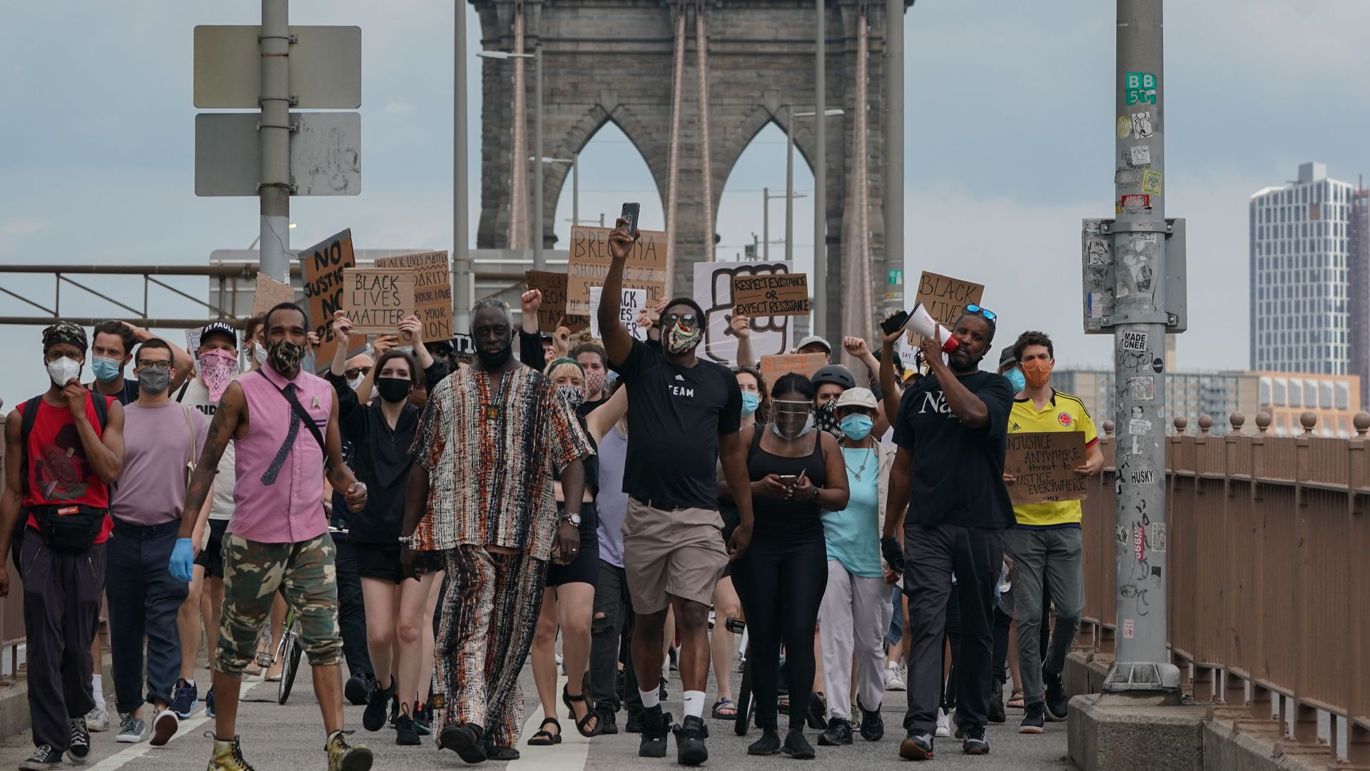 A group of masked protesters holding signs cross the Brooklyn Bridge in New York