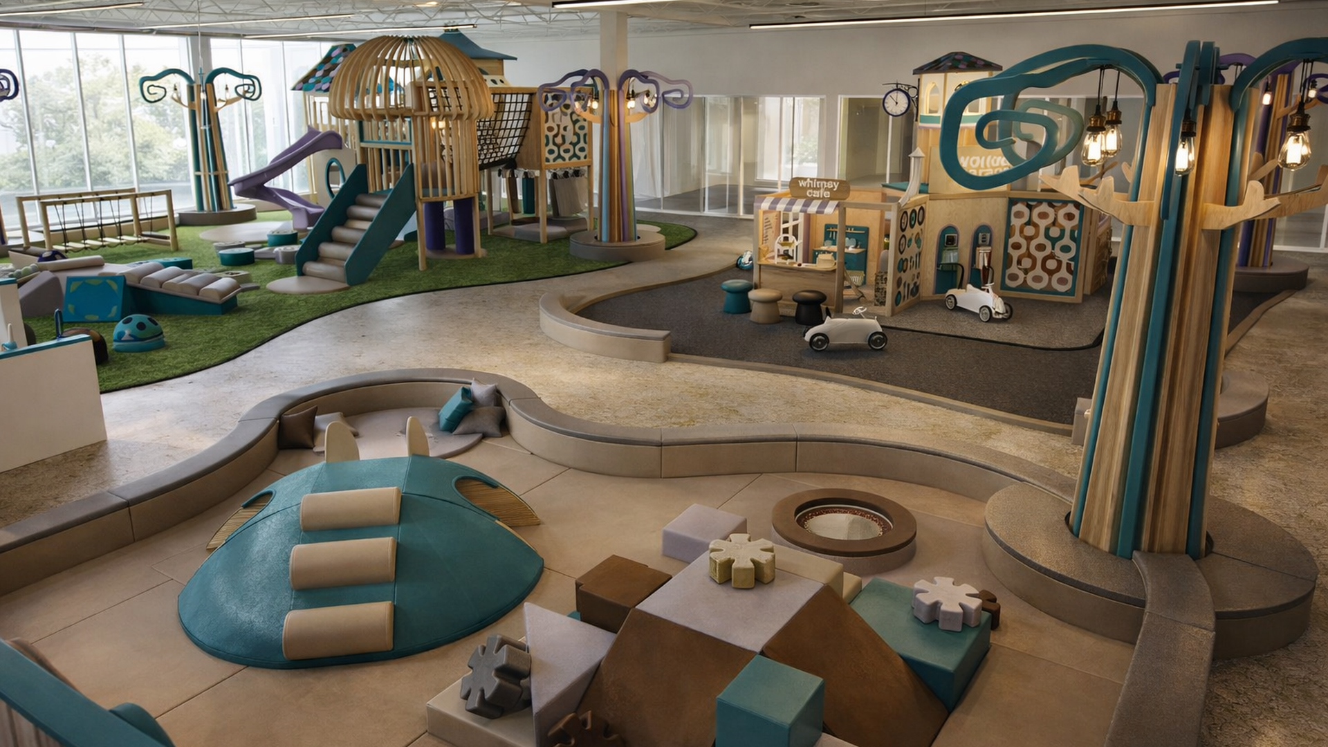 Indoor children's play area with a multi-level wooden climber, slides, soft teal and beige foam blocks, toy cars on a track, and large windows bringing in daylight.