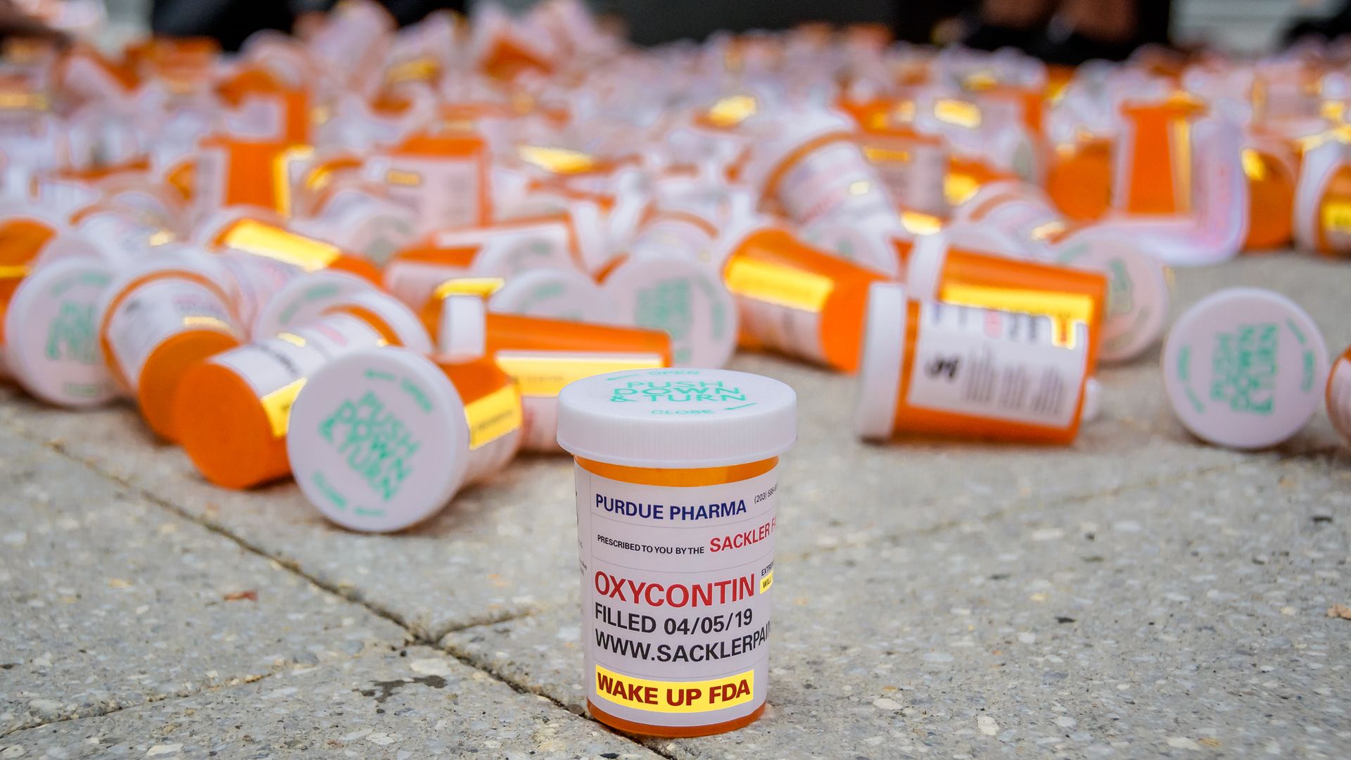 In this image, a pile of prescription bottles are piled on the concrete.
