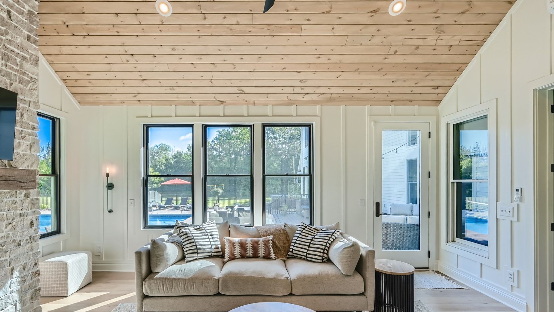A photo showing a family room with a couch, wooden ceiling and vertical, shiplap-like walls with black window casings