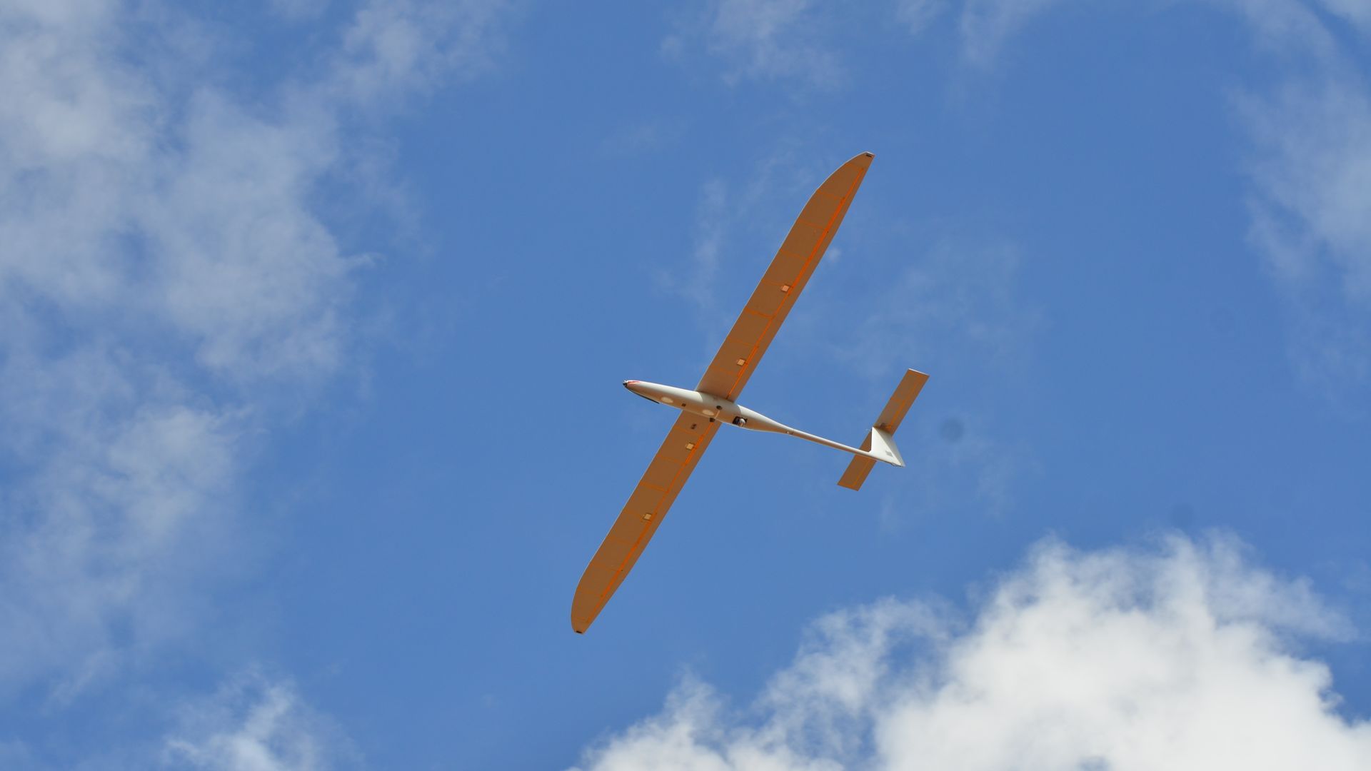 A photo shows a Kraus Hamdani Aerospace drone from below, flying beneath a blue sky.