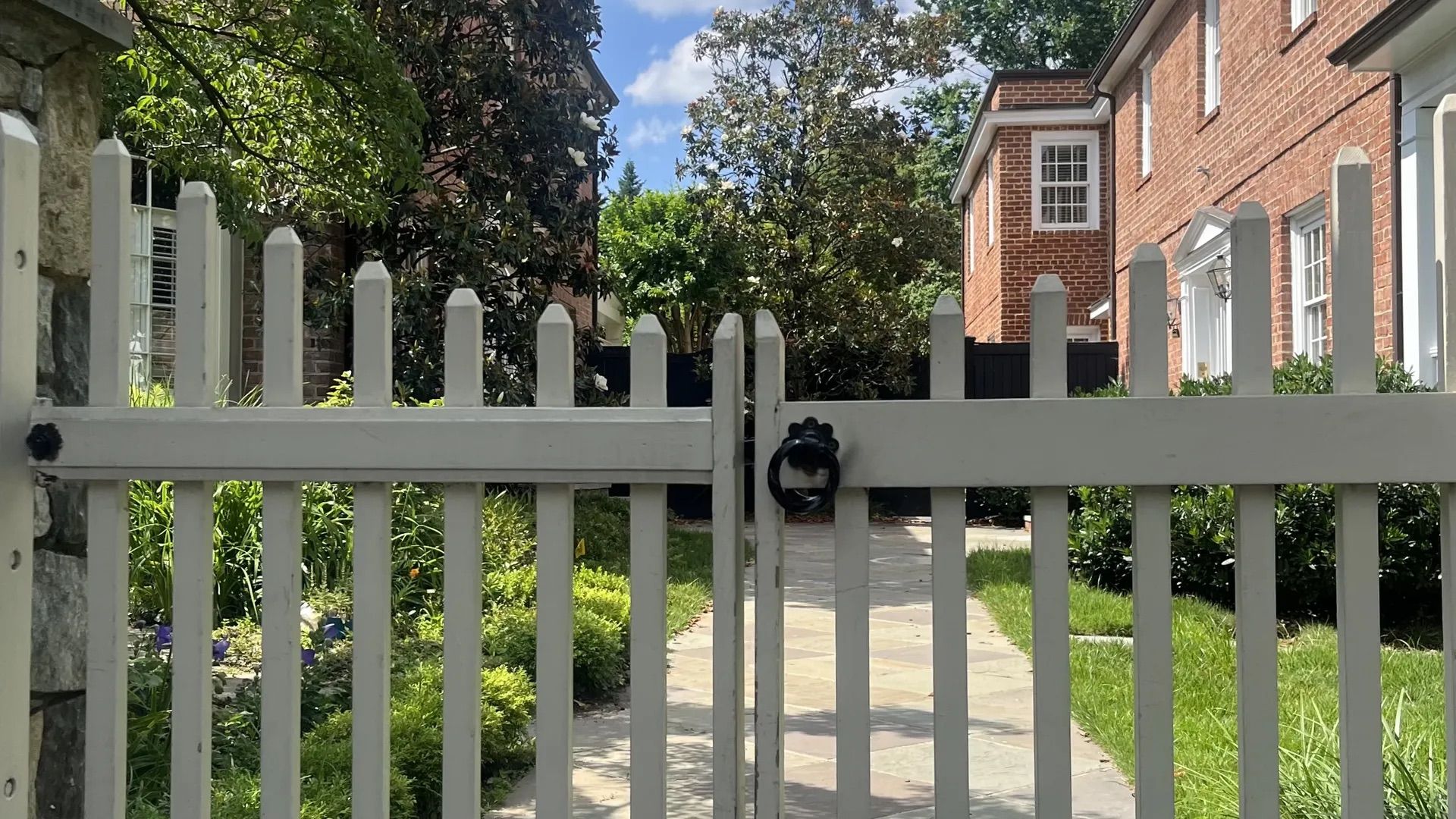 A photo showing a white picket gate, with a brick home in the background.