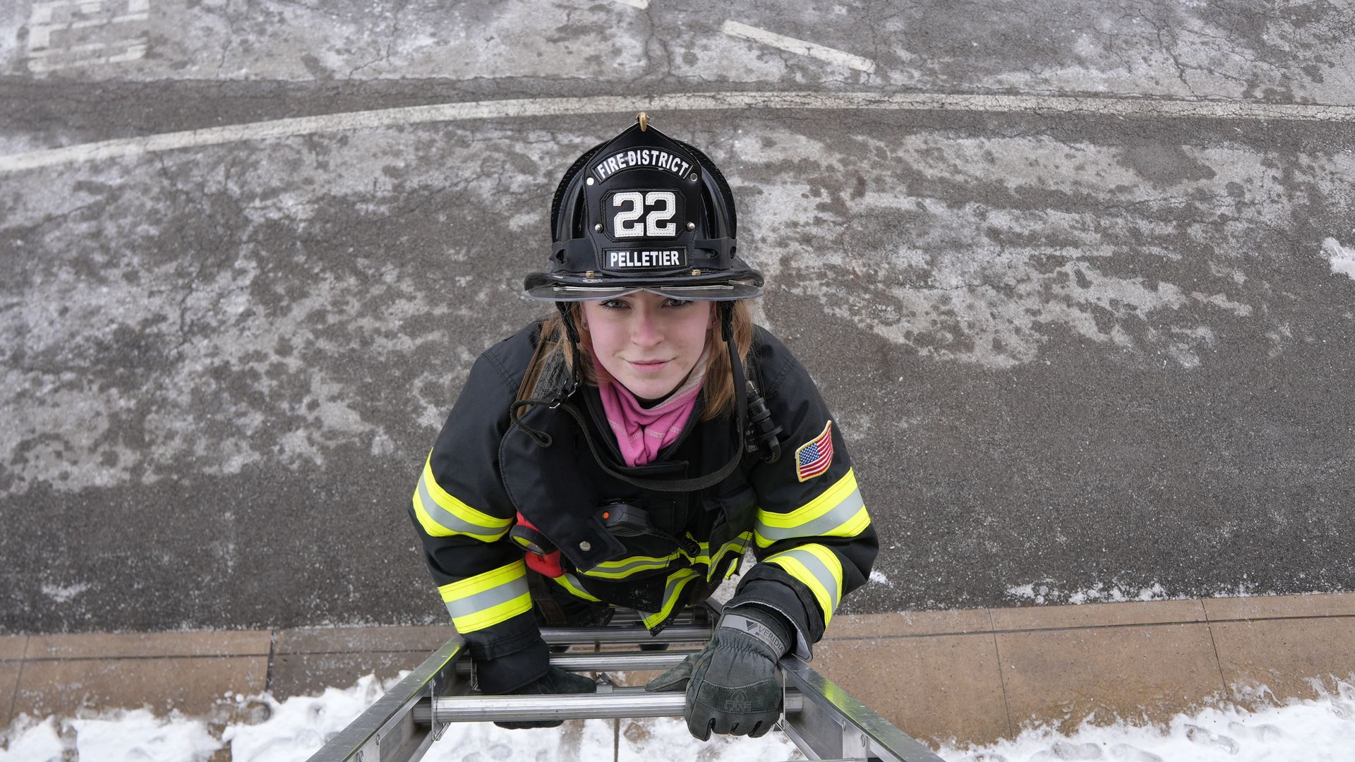 A firefighter smiles at the camera while climbing up a ladder.