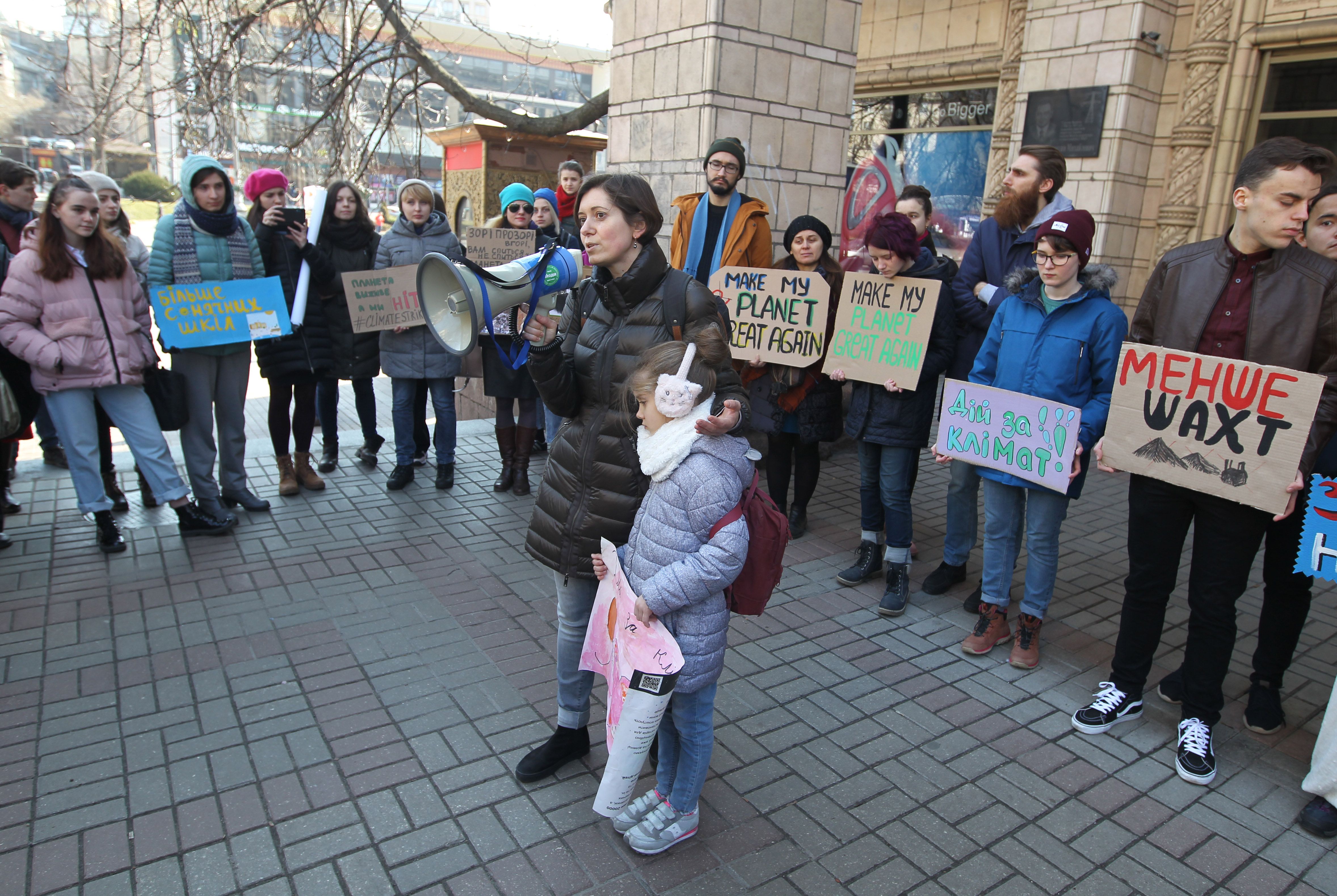 A circle of protestors stand around a woman with a bullhorn, who talks into it while holding a small child. 