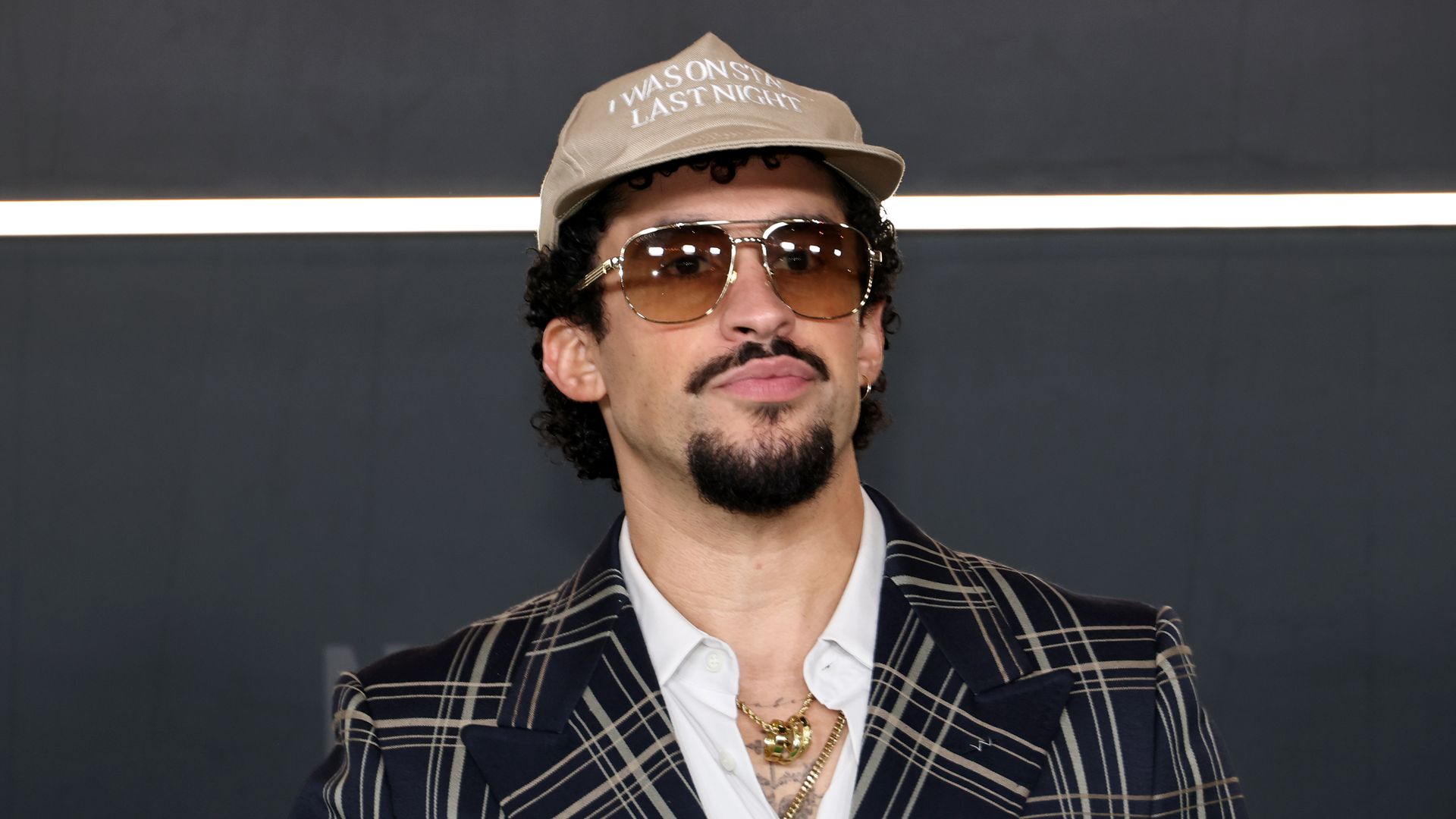 Bad Bunny wearing sunglasses, a suit and a hat at the premiere of "Happy Gilmore 2"