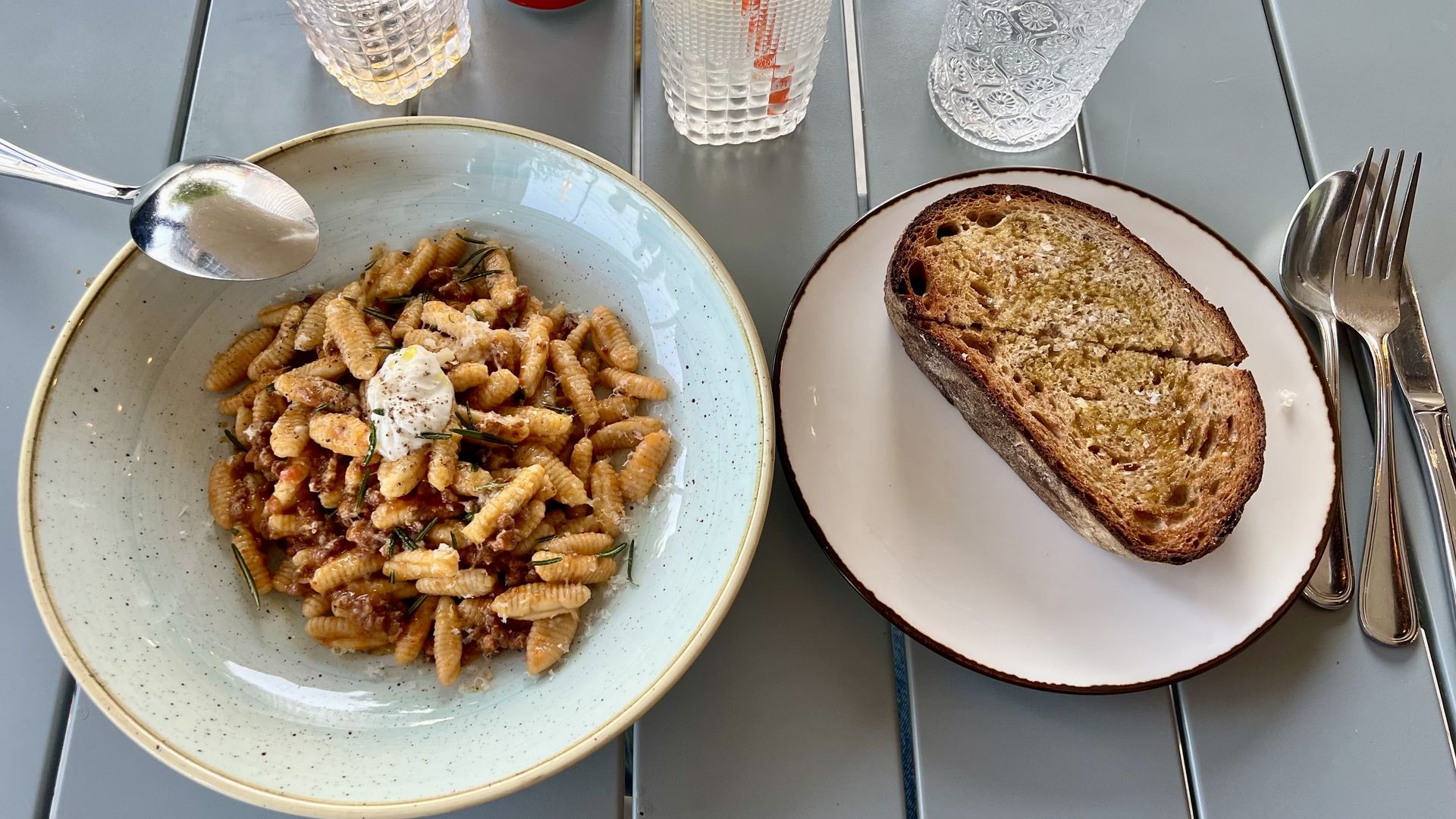 A photo of two plates on a table, the one of the left is a bowl of pasta withe whipped ricotta on top.