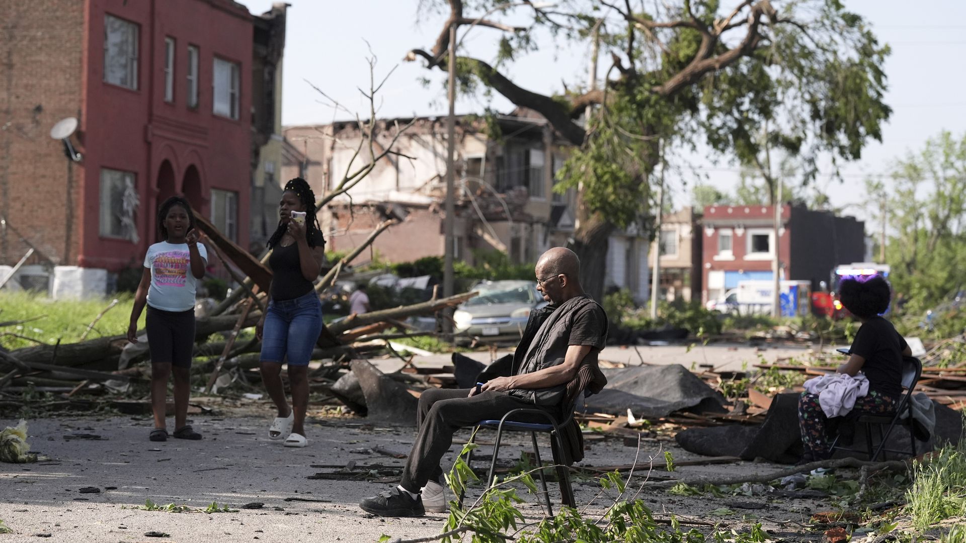 Man sits with storm damage around him and three other observers 