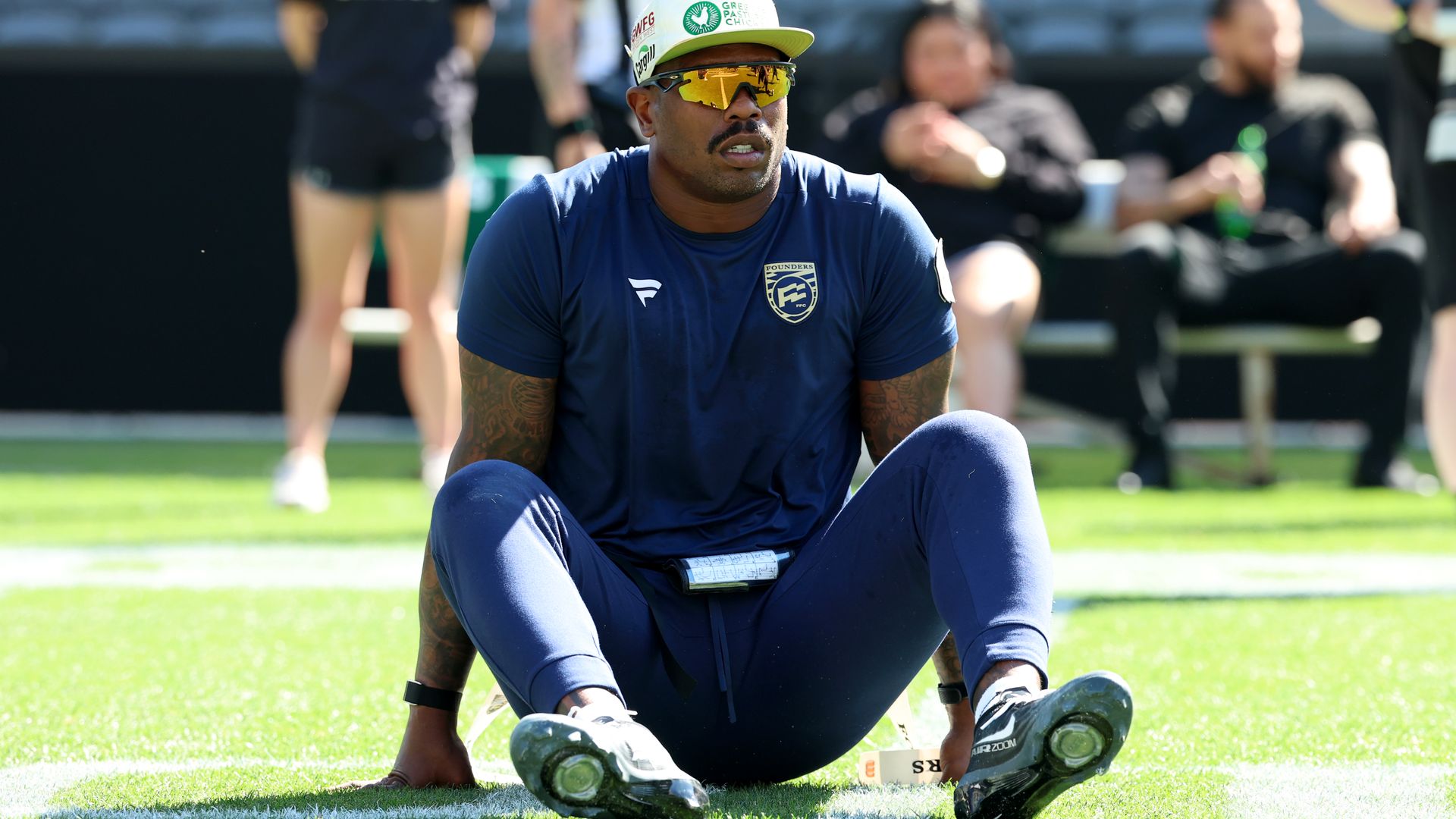 Von Miller sits on a field wearing cleats and sunglasses.