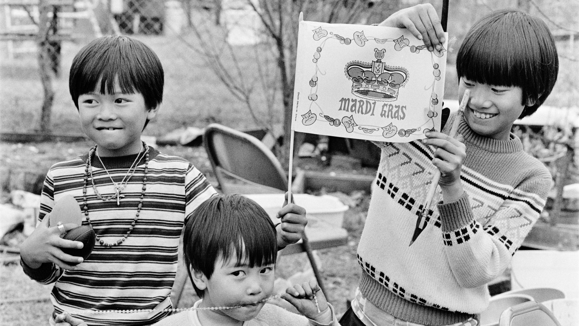 Three young boys smile as they play with Mardi Gras beads and a Mardi Gras flag.