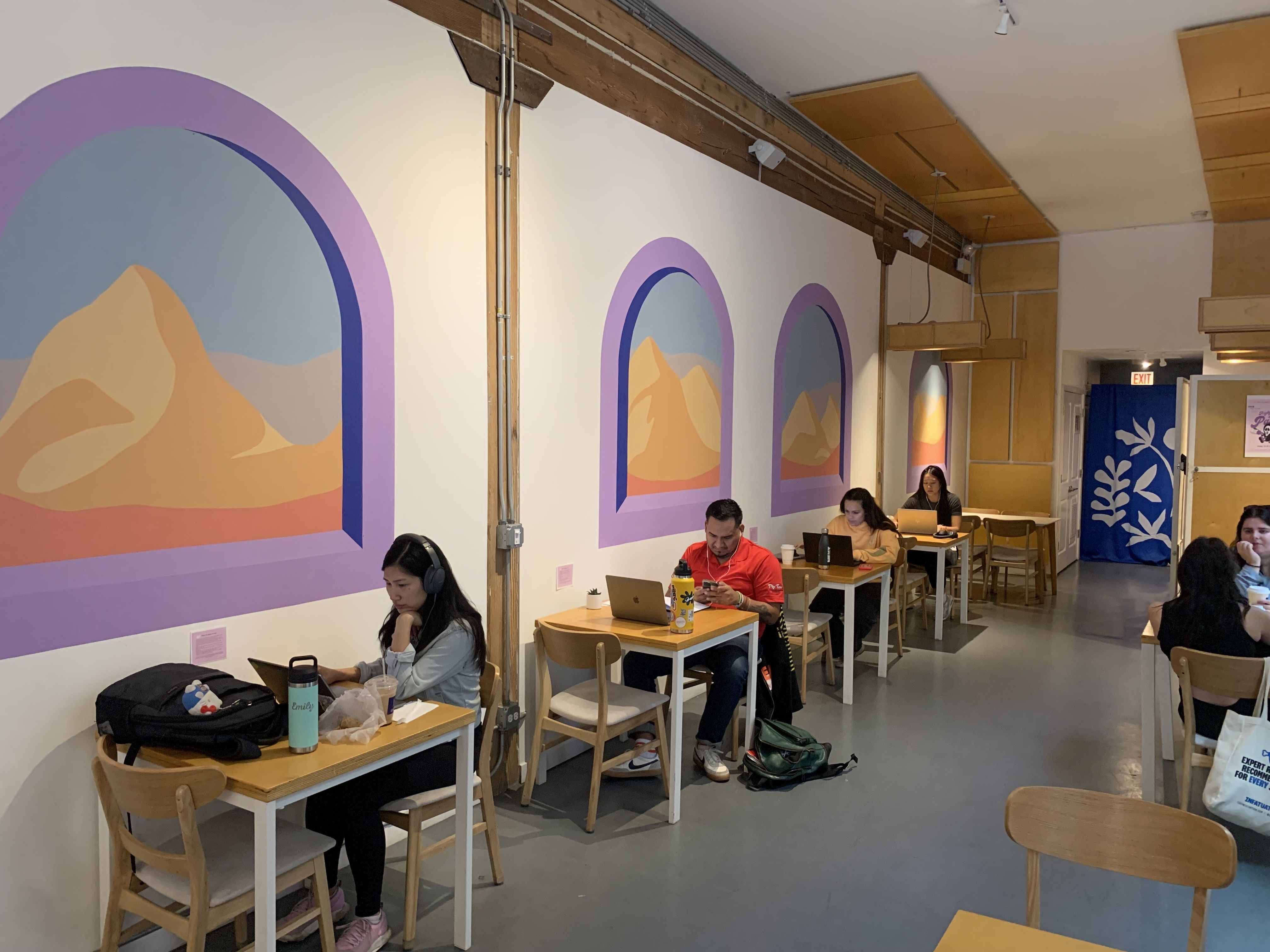 Photo of a coffee shop with people sitting at tables looking at computers 