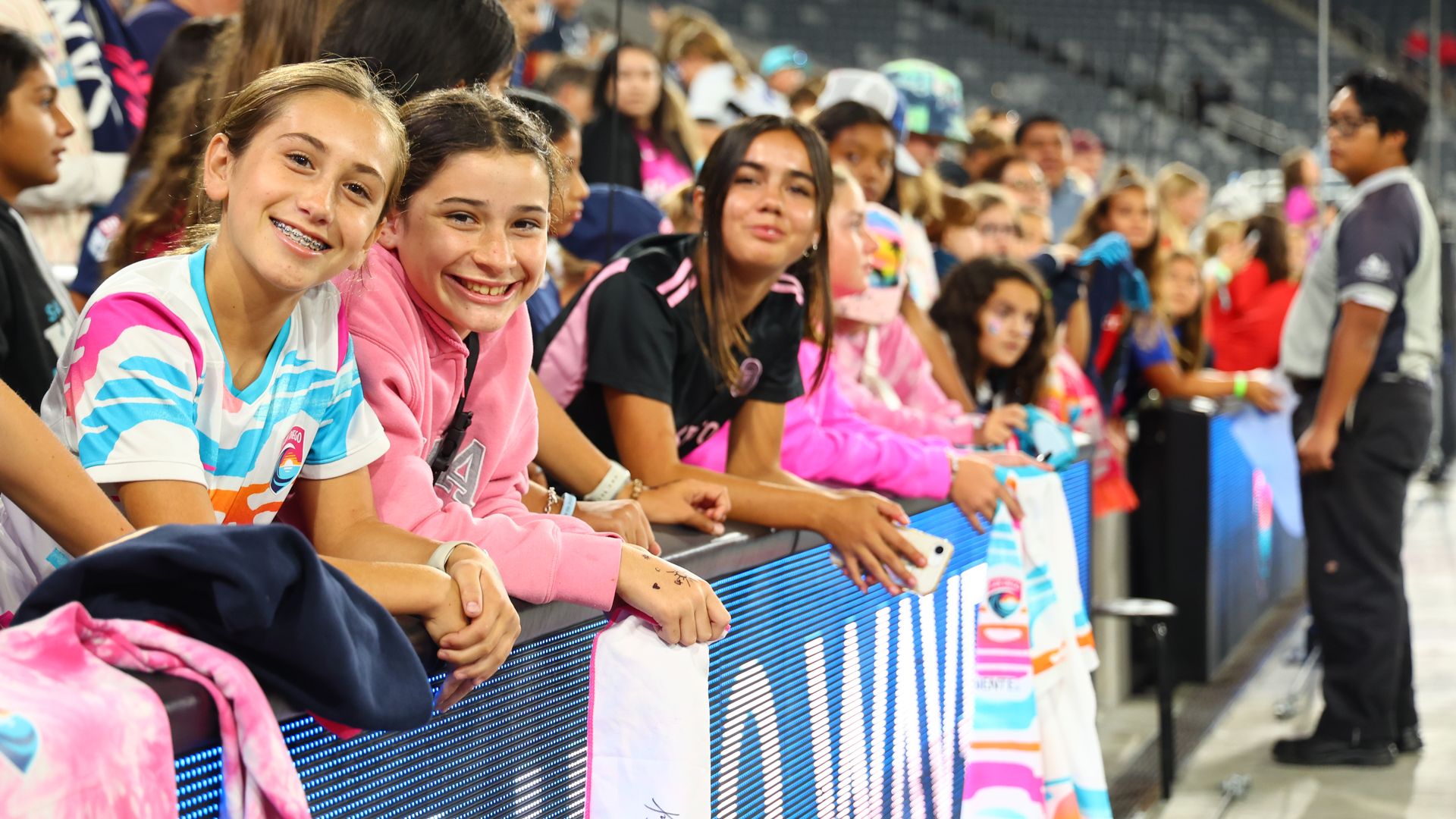 Young girls and fans of San Diego Wave smile while waiting in the stands to meet and get autographs from the players after a game.