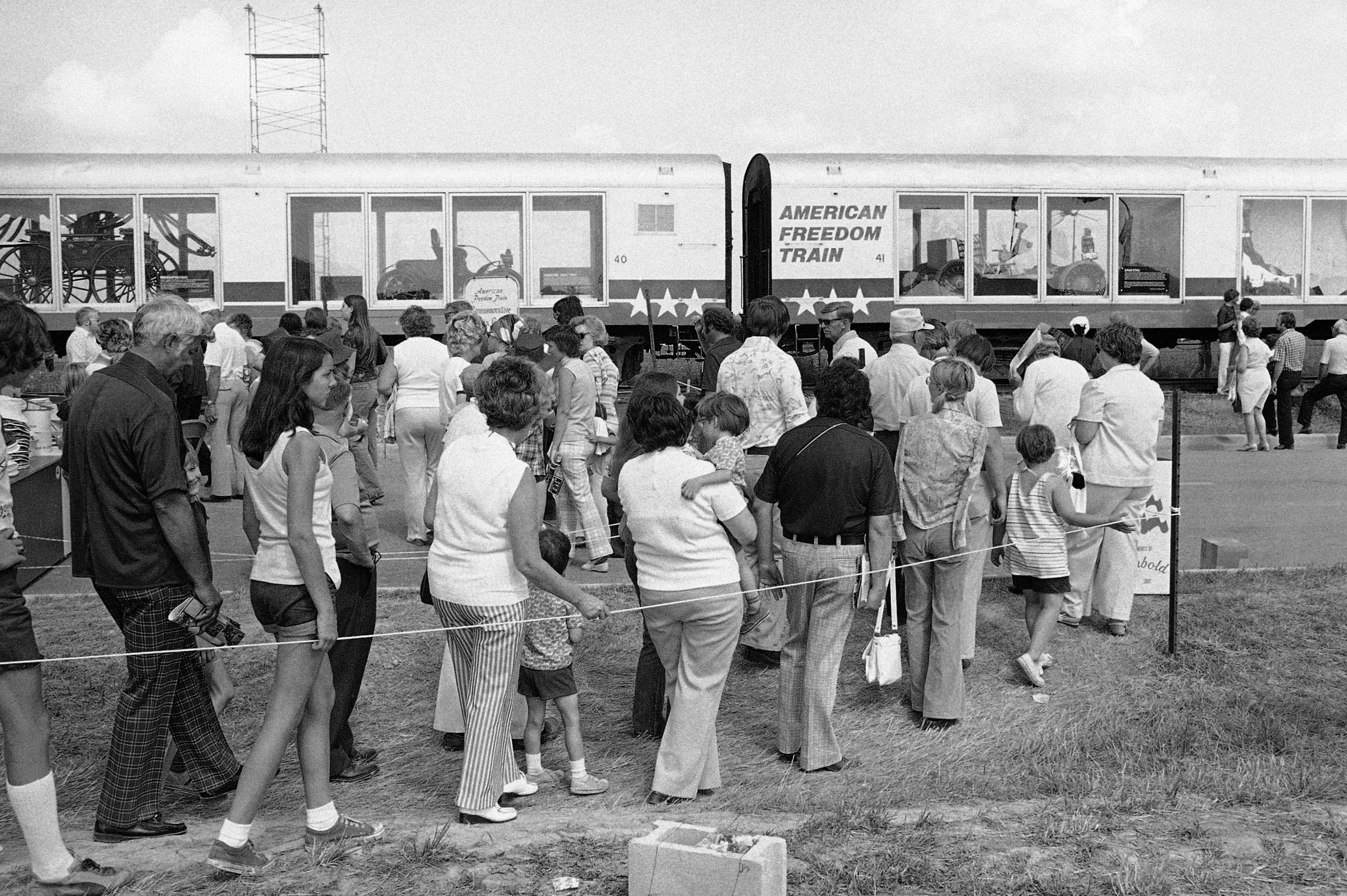 People line up to look at a train in a black and white photo