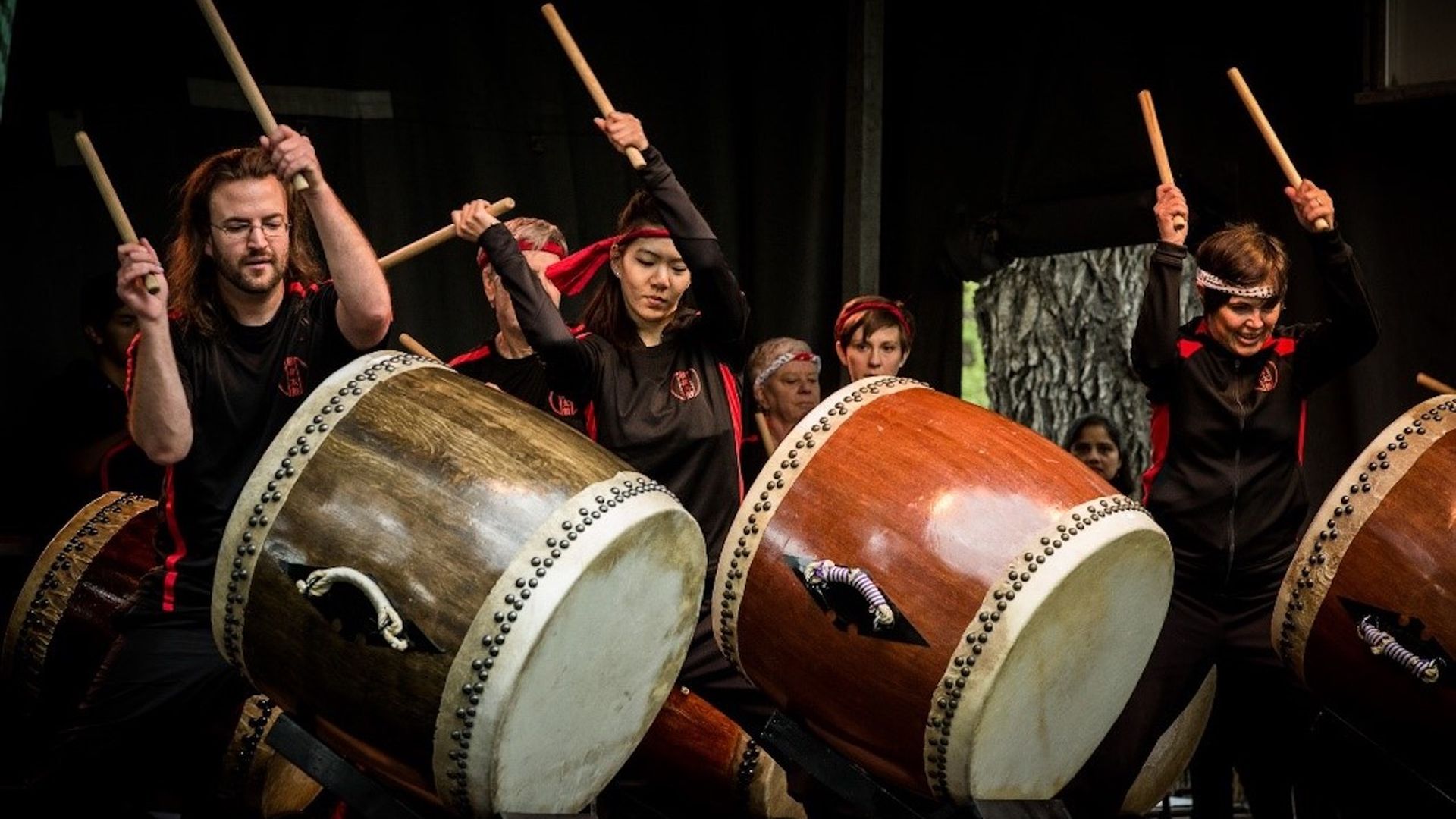 Drummers perform in a group on a black stage.