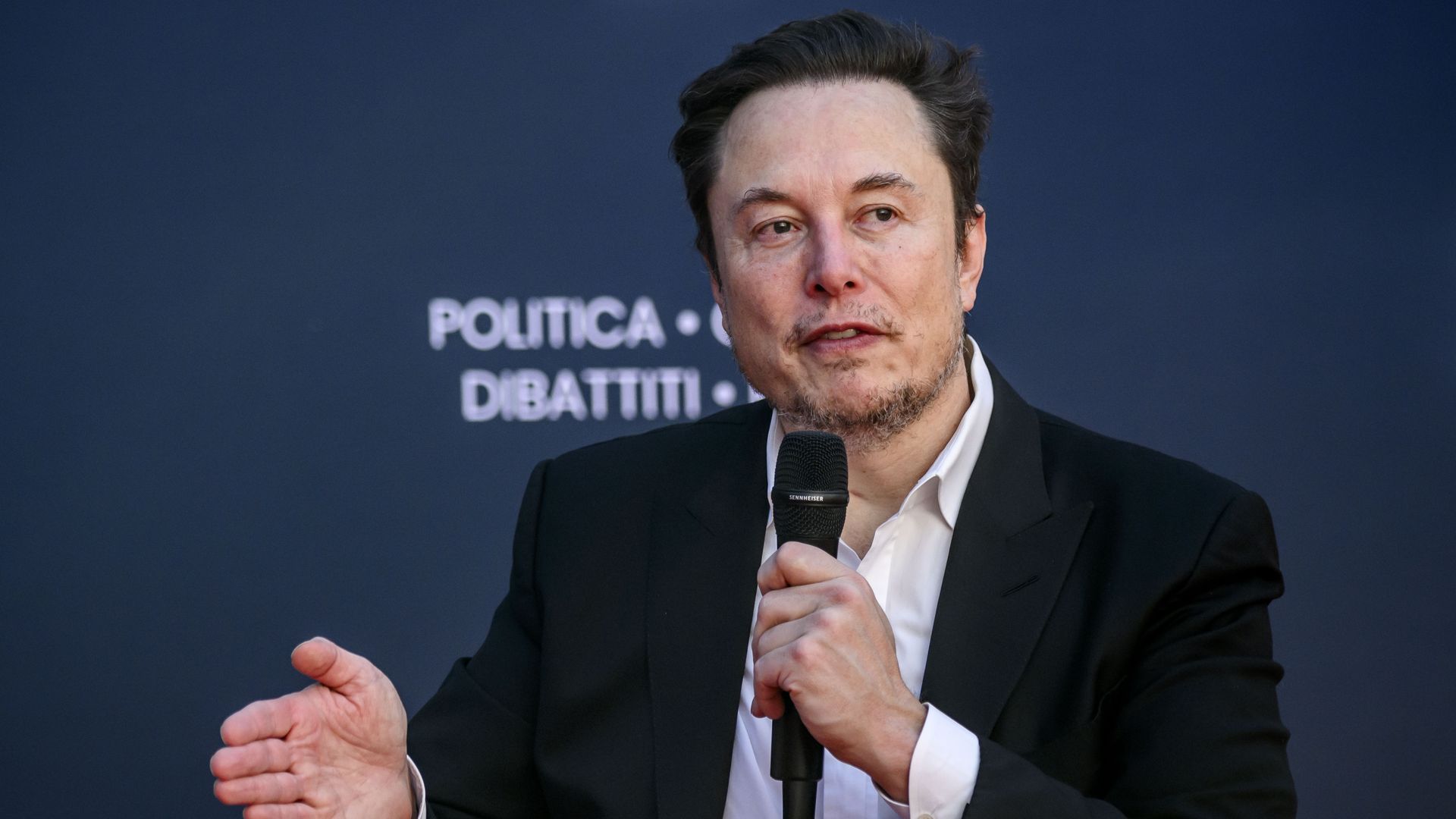 Elon Musk holds microphone while speaking at a convention