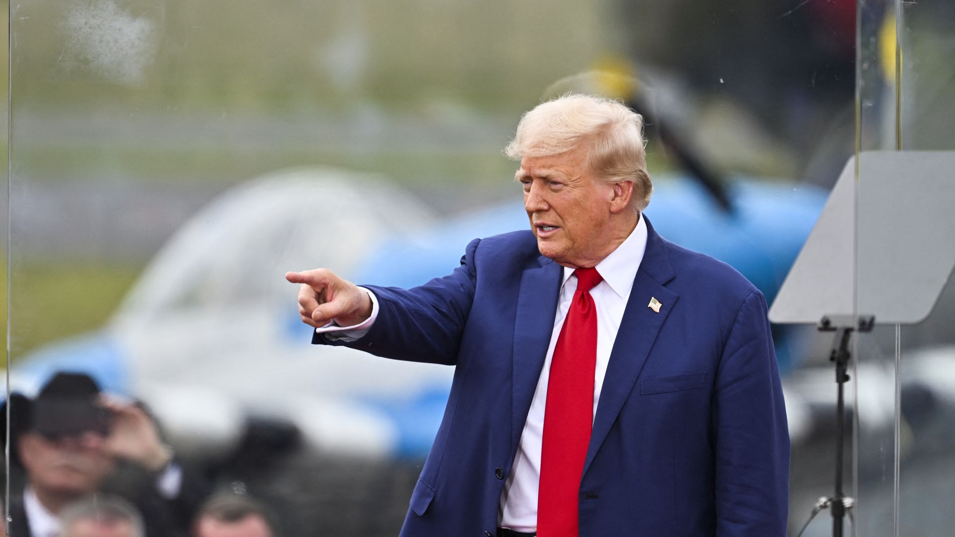 Donald Trump, wearing a blue suit, white shirt and red tie, points at a rally 