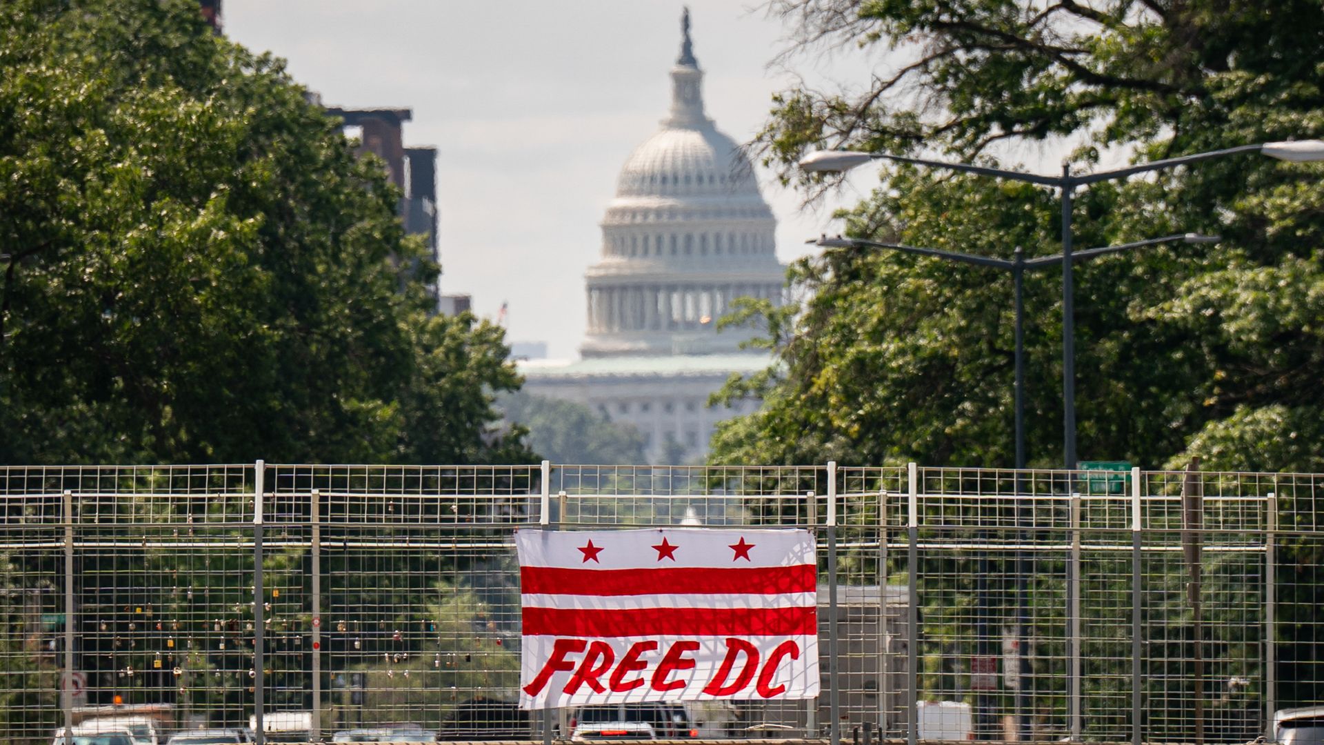 A D.C. flag with the words "FREE DC" scrawled in red below its red bars is hanging on a overpass with the U.S. Capitol building in the far background