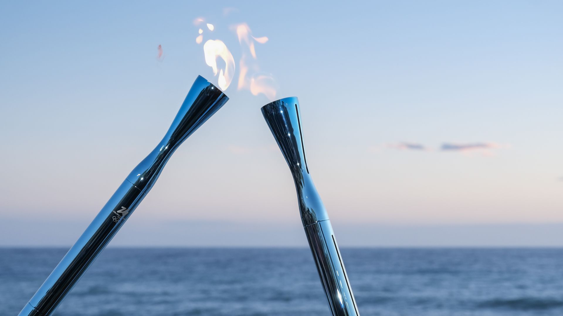Two Olympic torches pass a flame in front of an ocean