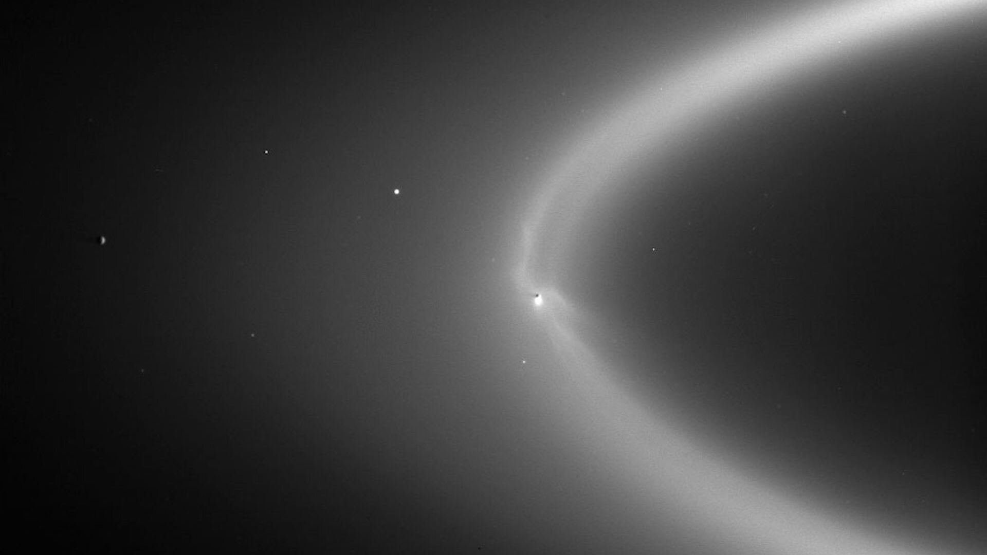 A black and white image of Saturn’s E ring being fed with icy particles from Enceladus’ plume.