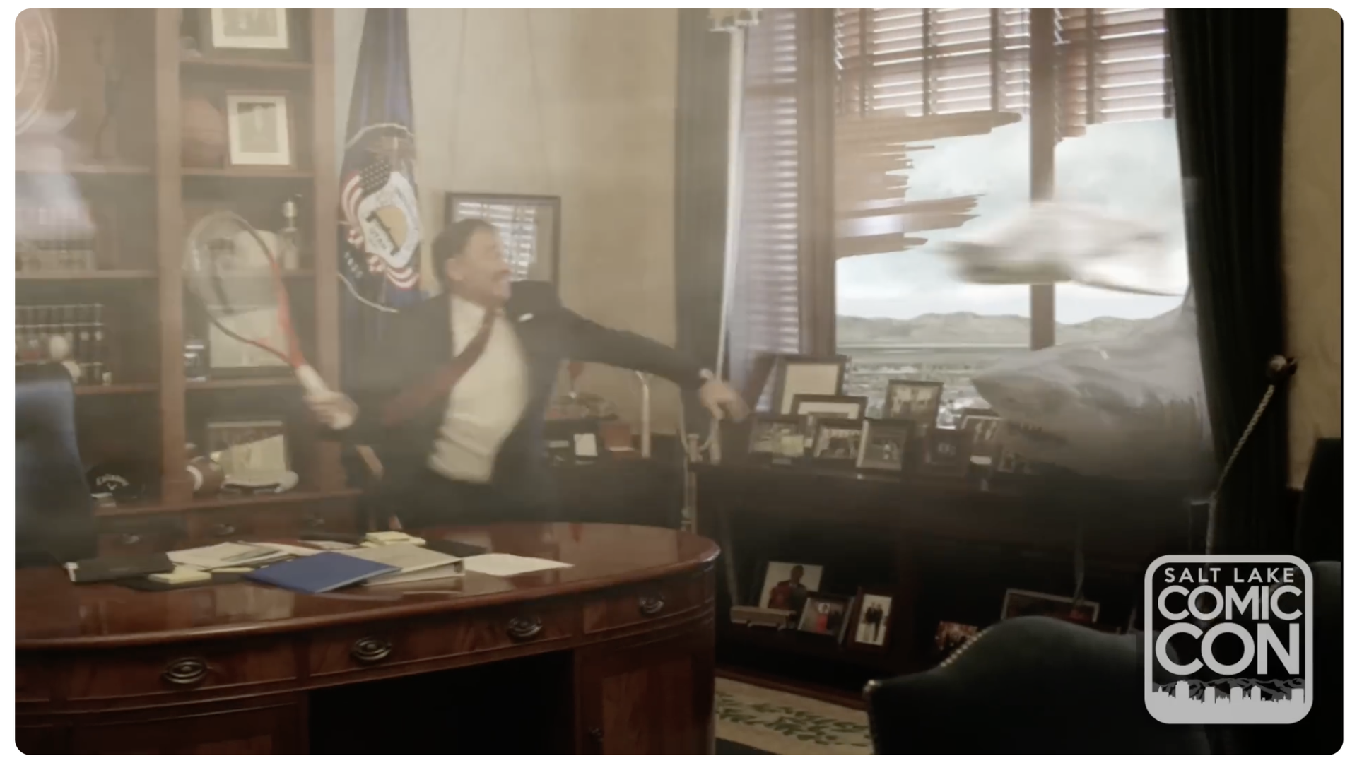 Man in a suit in a wood-paneled office, arms outstretched as a whirlwind blasts through the window blinds; desk cluttered with papers and photos, Salt Lake Comic Con watermark.