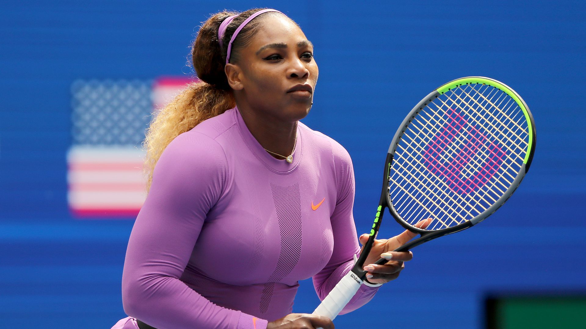 A woman in a pinkish shirt holds a tennis racket upright